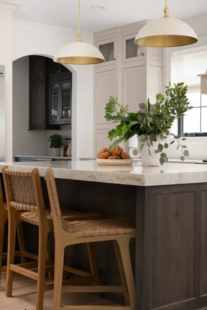 Modern kitchen with white and dark cabinetry, a marble countertop island, wooden barstools, and a green plant in a white vase.