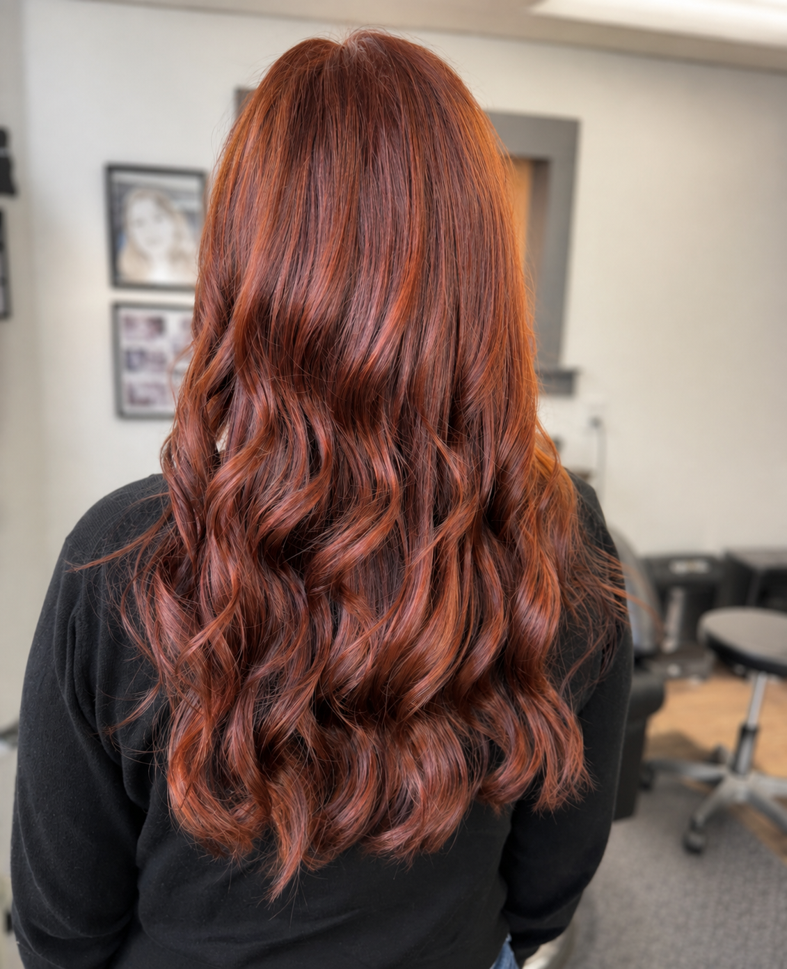 Back view of a woman with long, wavy, red hair in a salon or studio setting.