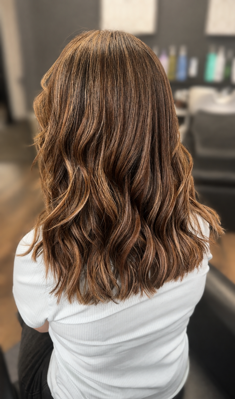 Back view of a woman with long, wavy, light brown hair in a salon setting.