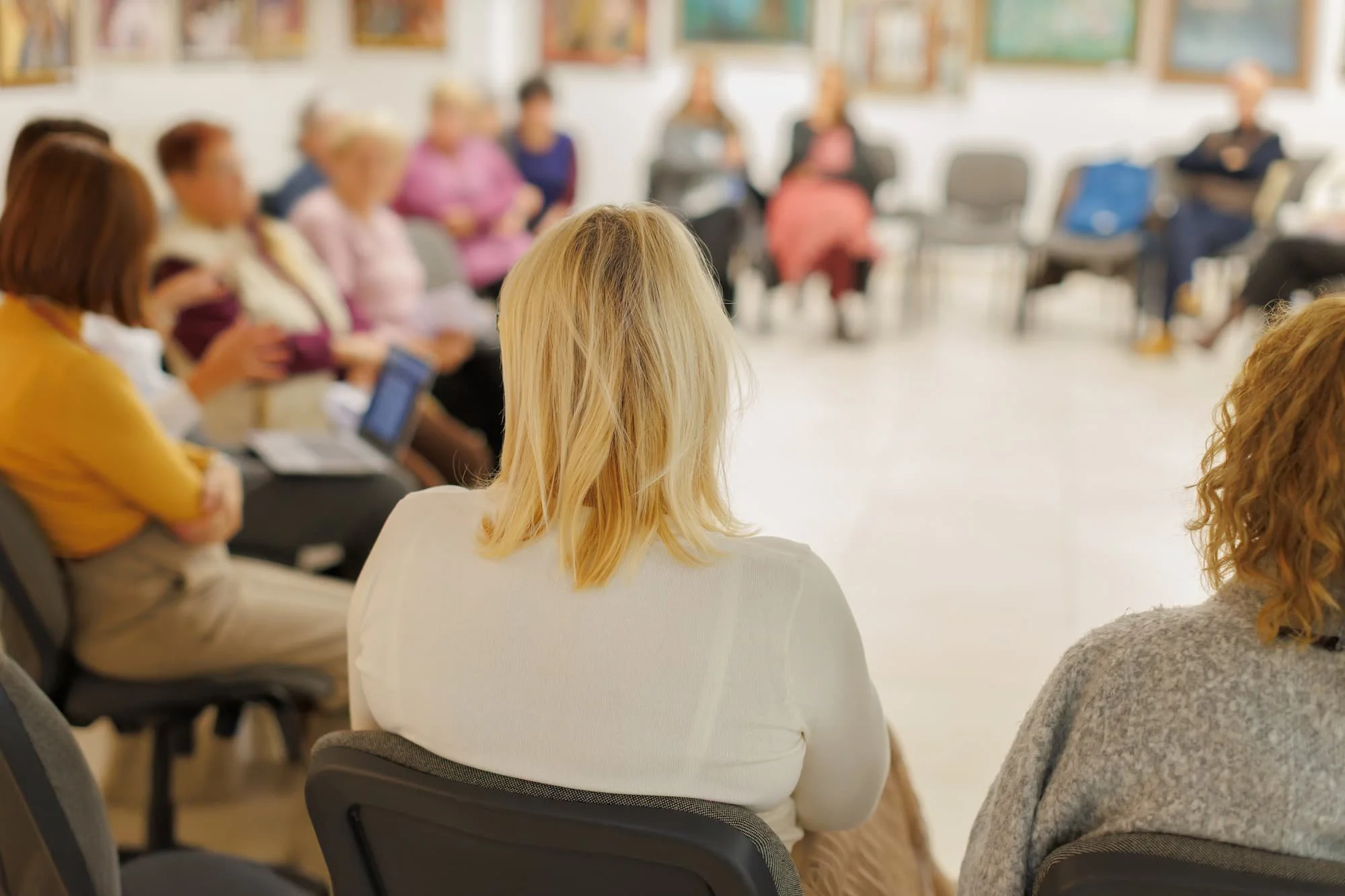 People sitting in chairs in a circle in a classroom or community room, participating in a group discussion or meeting.