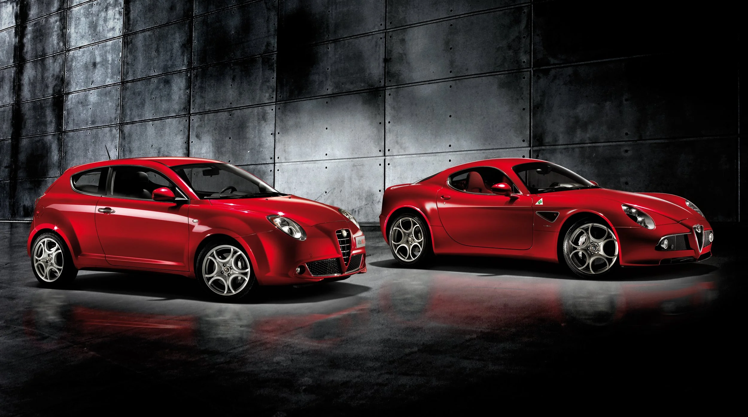 Press image of the Alfa Romeo Mito parked next to the Alfa Romeo 8C in a dark studio setting.