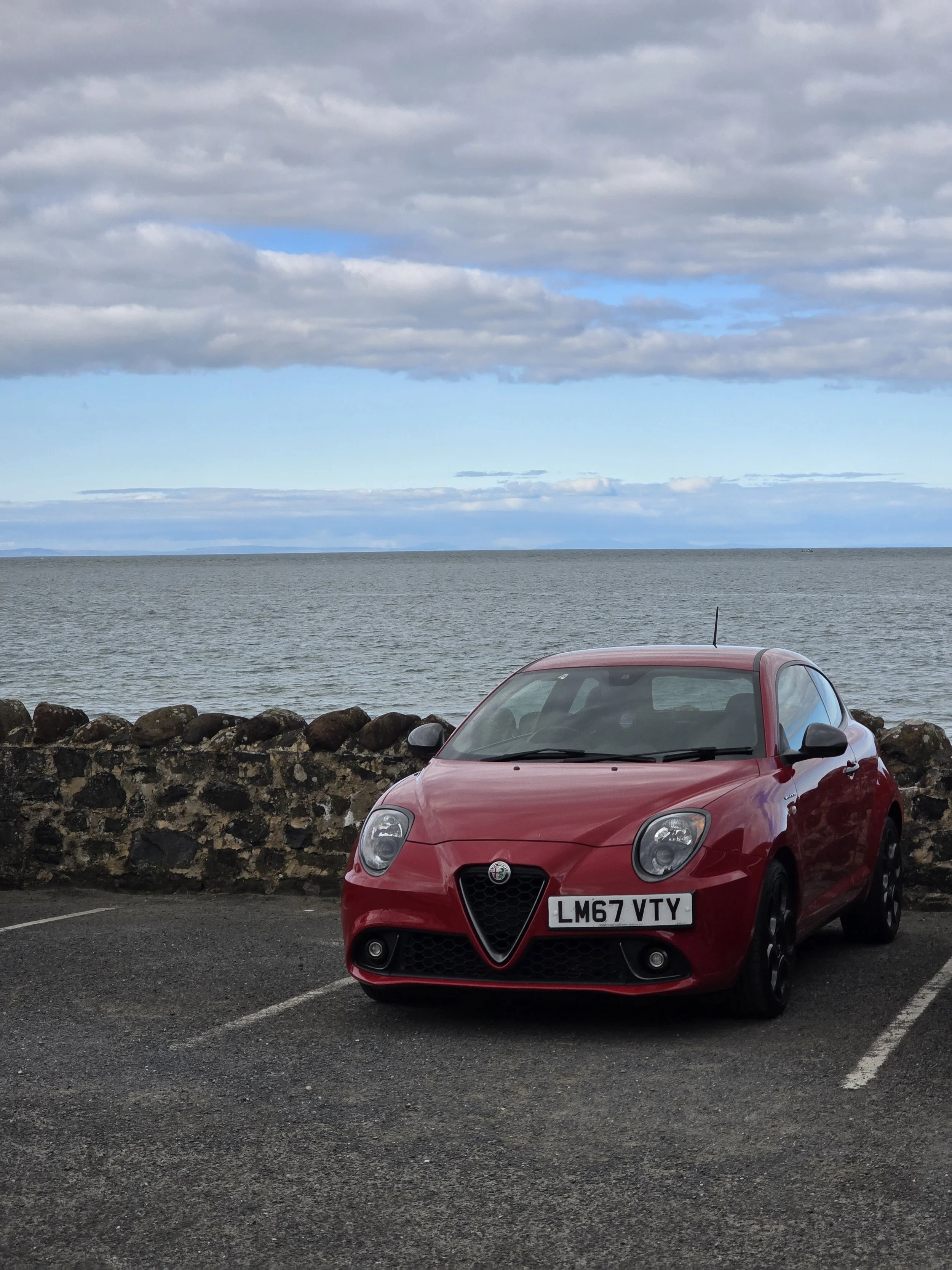 Red Alfa Romeo Mito parked facing away from the ocean.