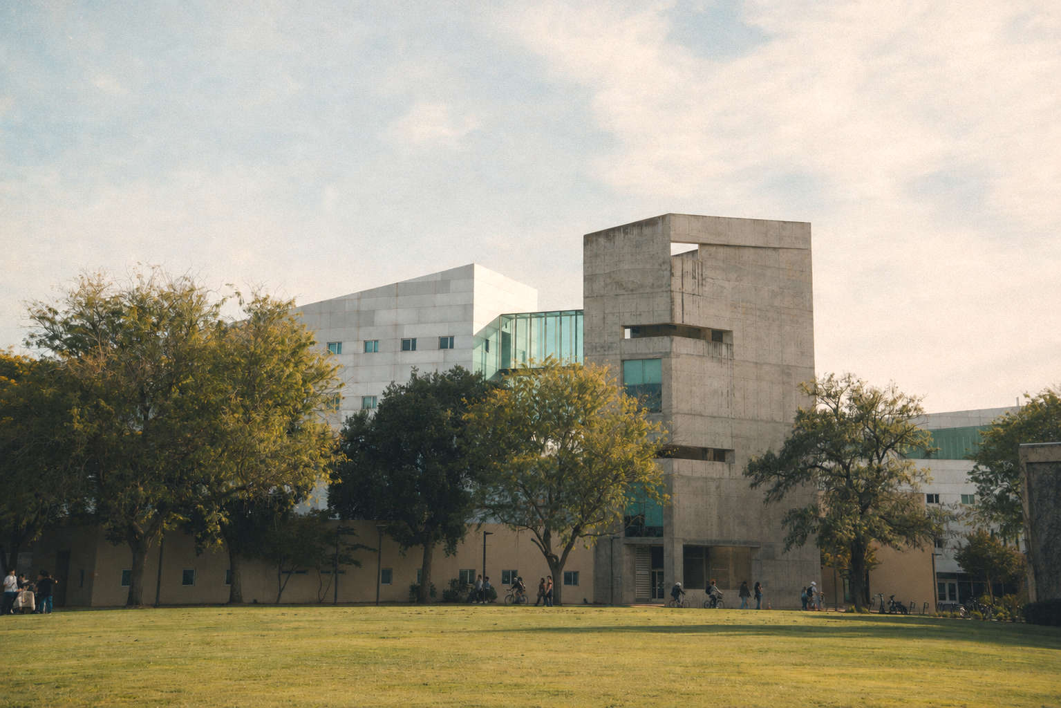 Modern concrete and glass building with trees and people walking and bicycling in front, under a partly cloudy sky. The Social Sciences building also known as the death star at UC Davis.