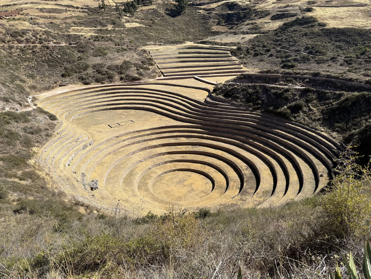 Ancient Incan terraced agricultural site on a hillside with concentric stone terraces surrounded by dry grass and shrubs.