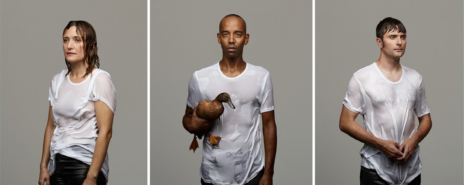 Triptych of theatre production photos showing three people in soaked white t-shirts against a grey background: a woman with wet hair on the left, a man holding a live duck in the centre, and a man with dripping wet hair on the right.