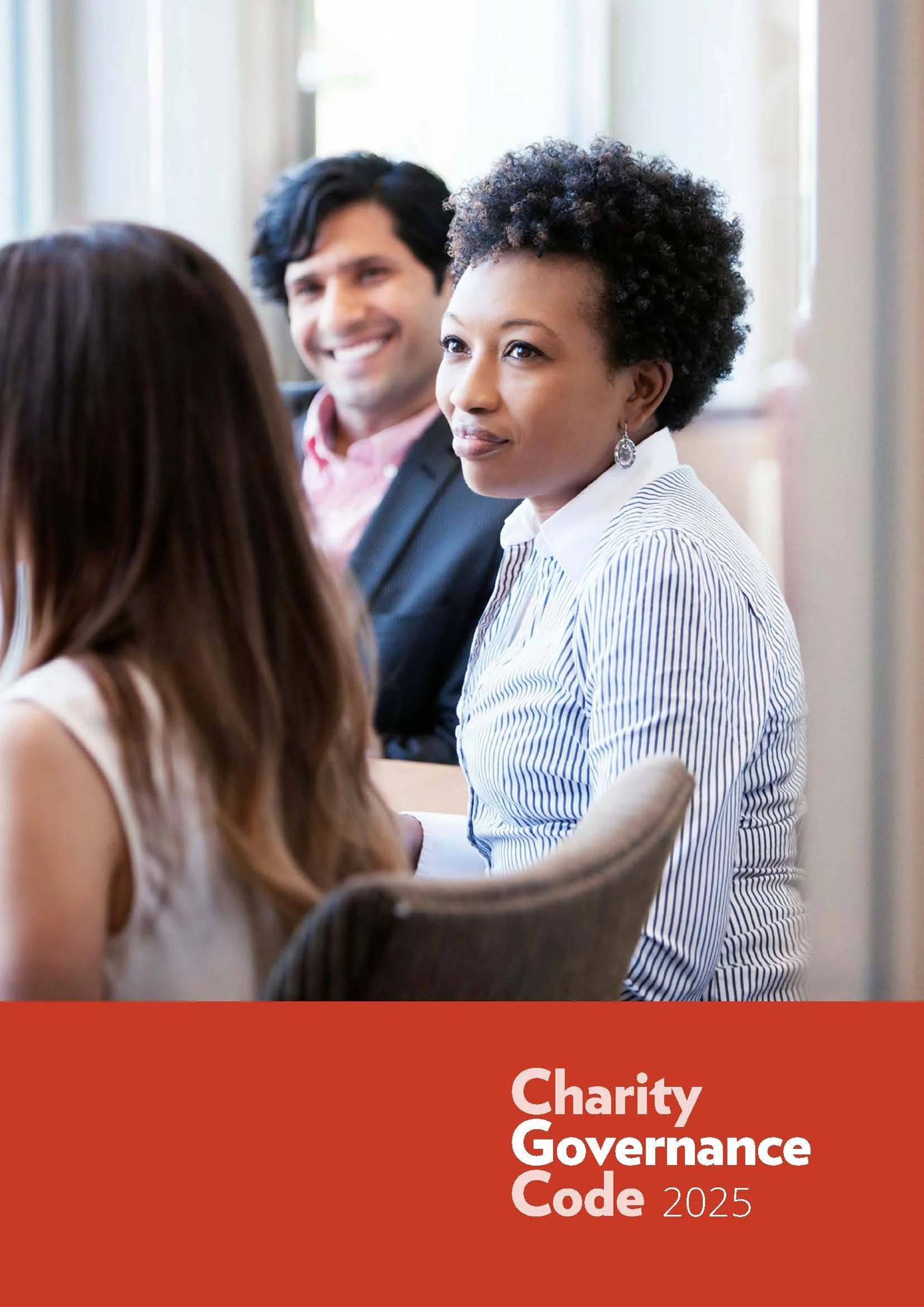 Cover of the "Charity Governance Code 2025" showing a woman in a striped shirt smiling and listening attentively in a meeting, with a man in the background and another person's back visible in the foreground, on a red banner at the bottom.
