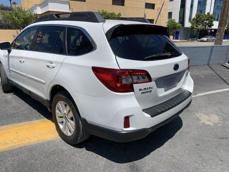 White Subaru Outback parked on city street, view of rear and driver's side.