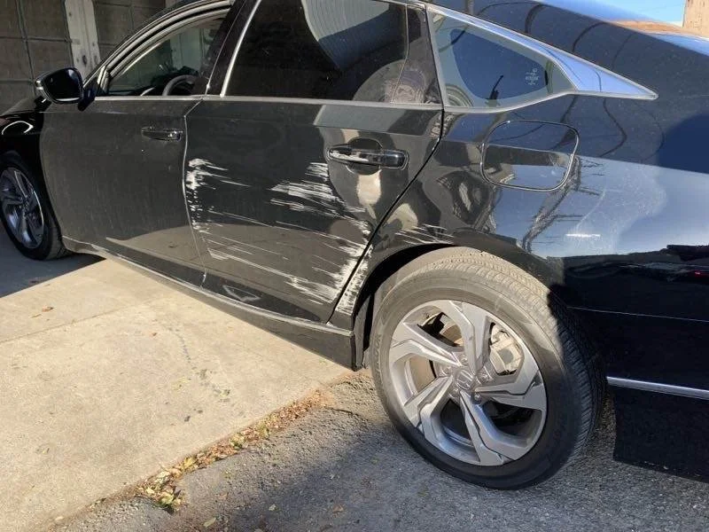 Black sedan with visible scratches and dents on the passenger side door.