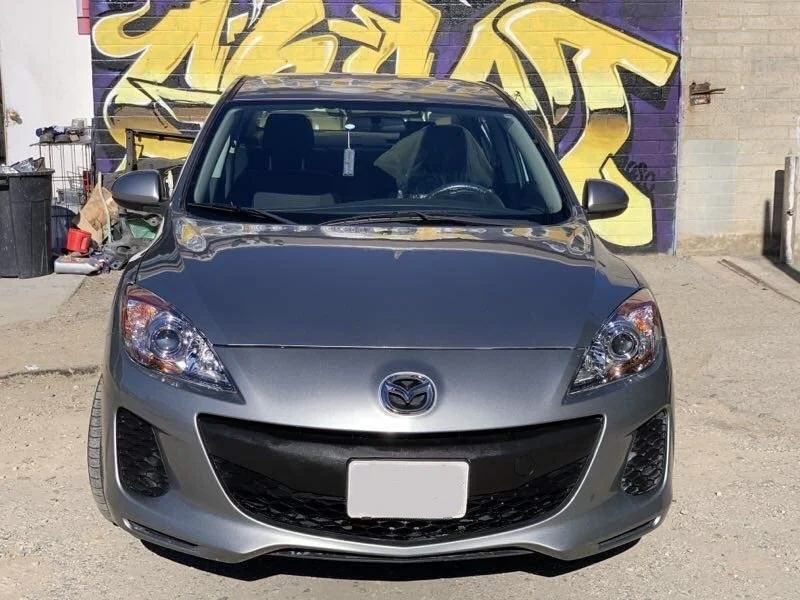 A silver Mazda sedan parked in front of a graffiti-covered wall.