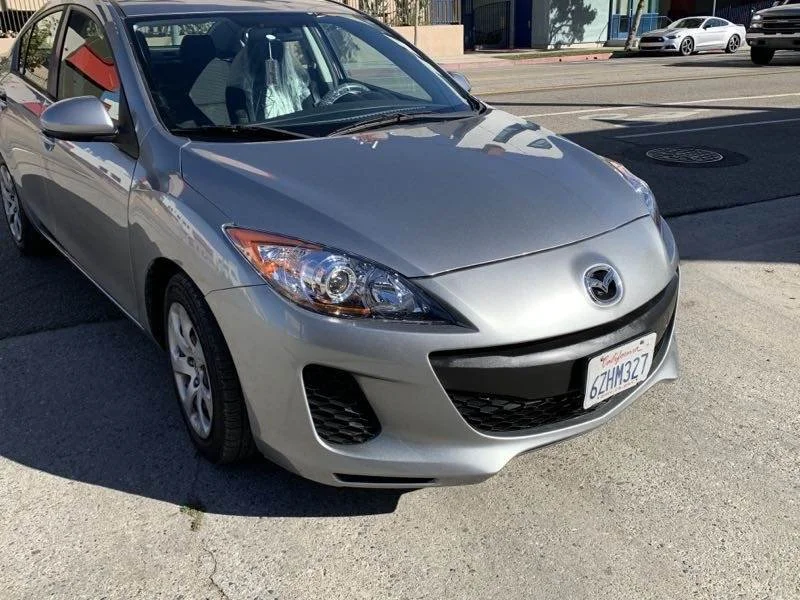 Silver Mazda sedan parked on the street with other vehicles and buildings in the background.