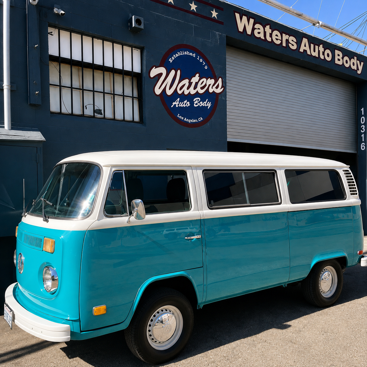 A vintage blue and white Volkswagen camper van parked in front of Waters Auto Body, a store in Los Angeles, California. The store has a sign on the wall and a large rolling door.