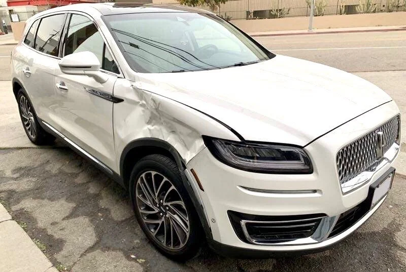 White Honda SUV with front-end damage parked on a city street.