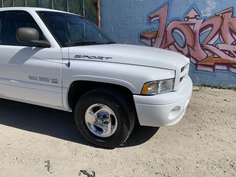 White Dodge Ram 1500 V8 truck parked on dirt with graffiti on the blue wall in the background.