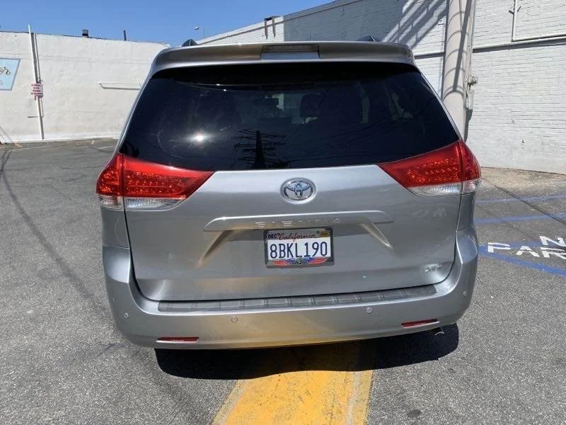 Rear view of a silver Toyota Sienna minivan with a California license plate 8BKL190, parked in a parking lot next to a white wall.