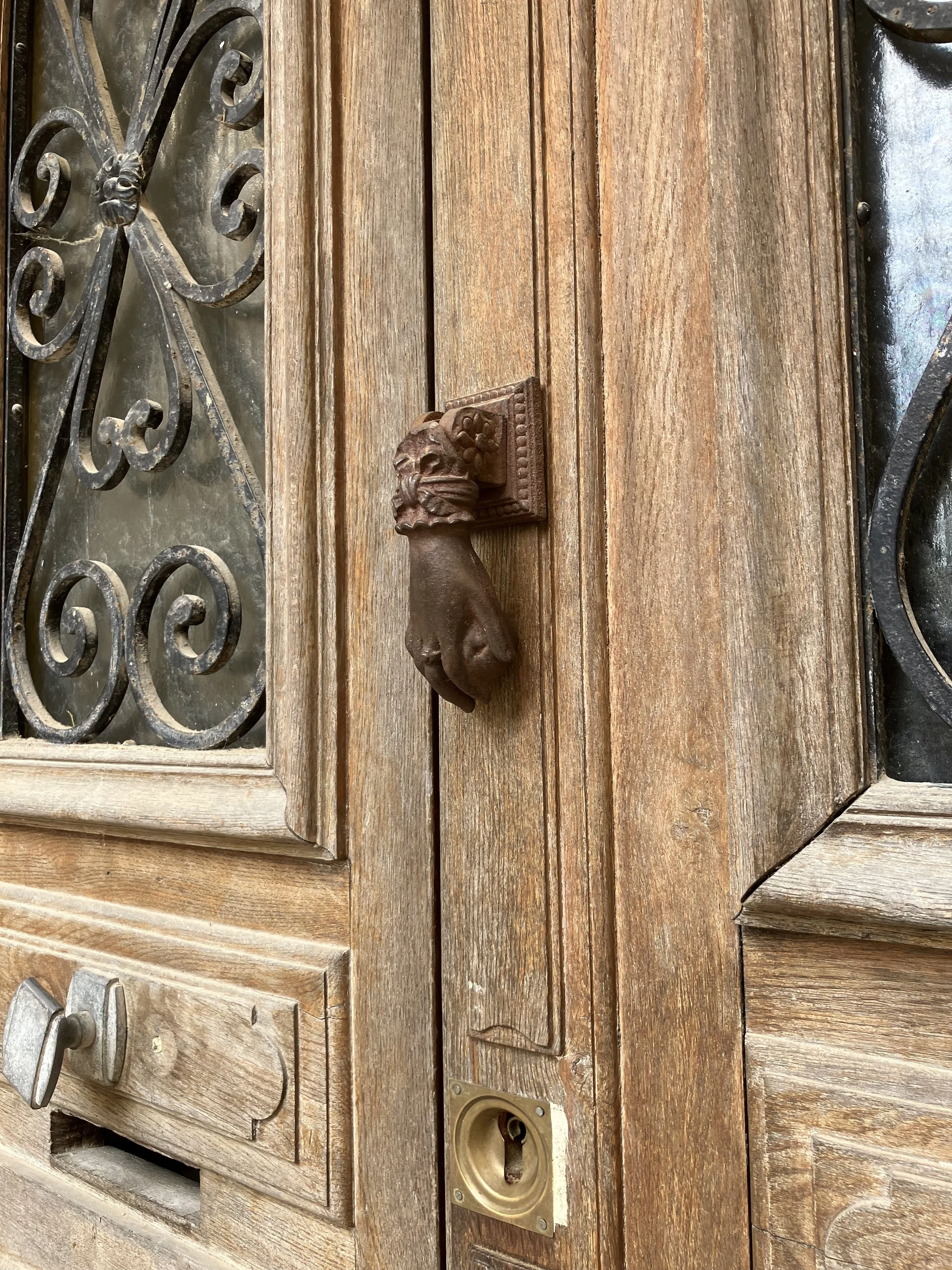 Close-up of a rustic wooden door with a lion head door handle and an ornate metal grille on the window