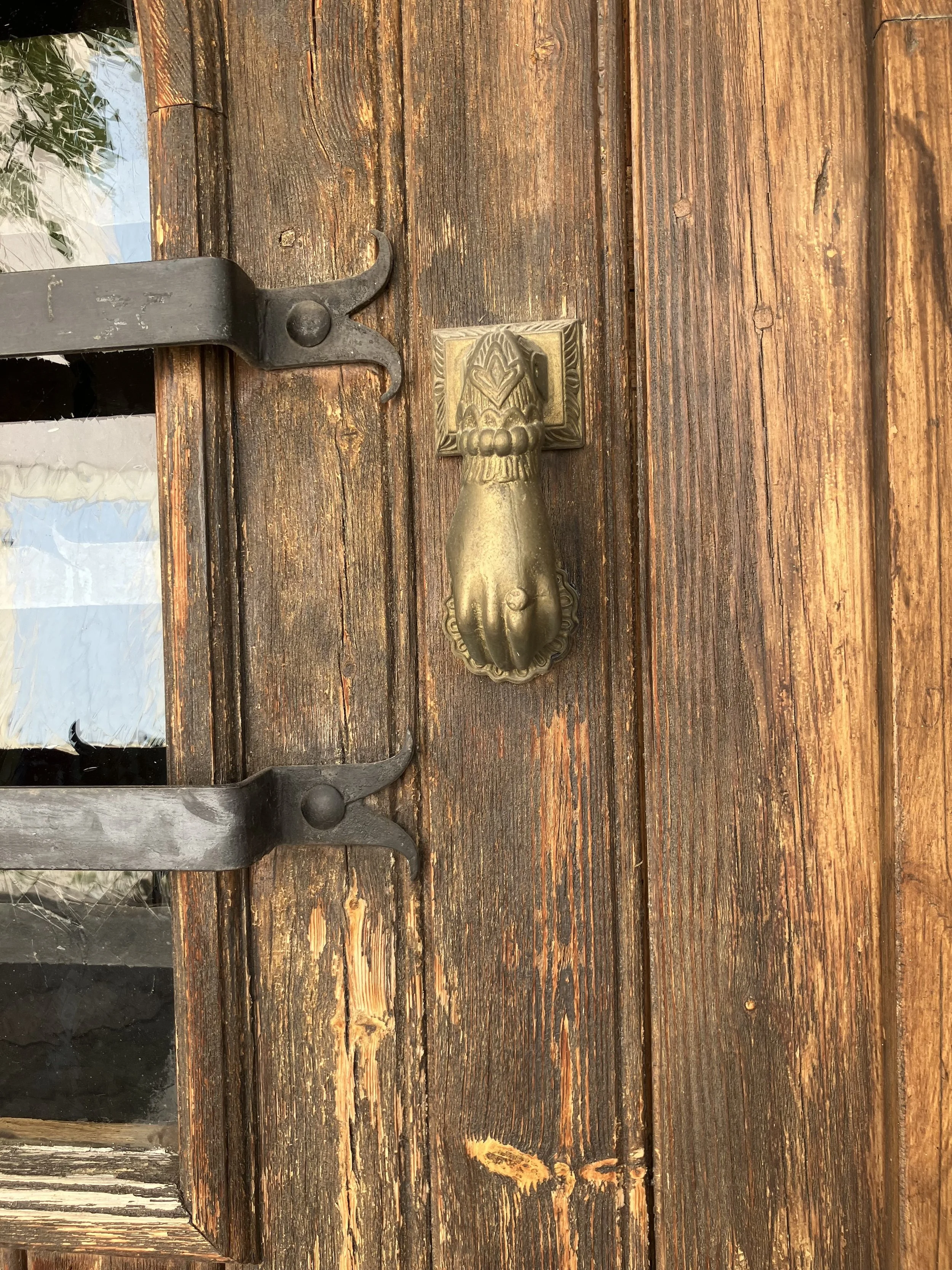 Close-up of a rustic wooden door with a vintage brass lion head door knocker and a black metal latch.