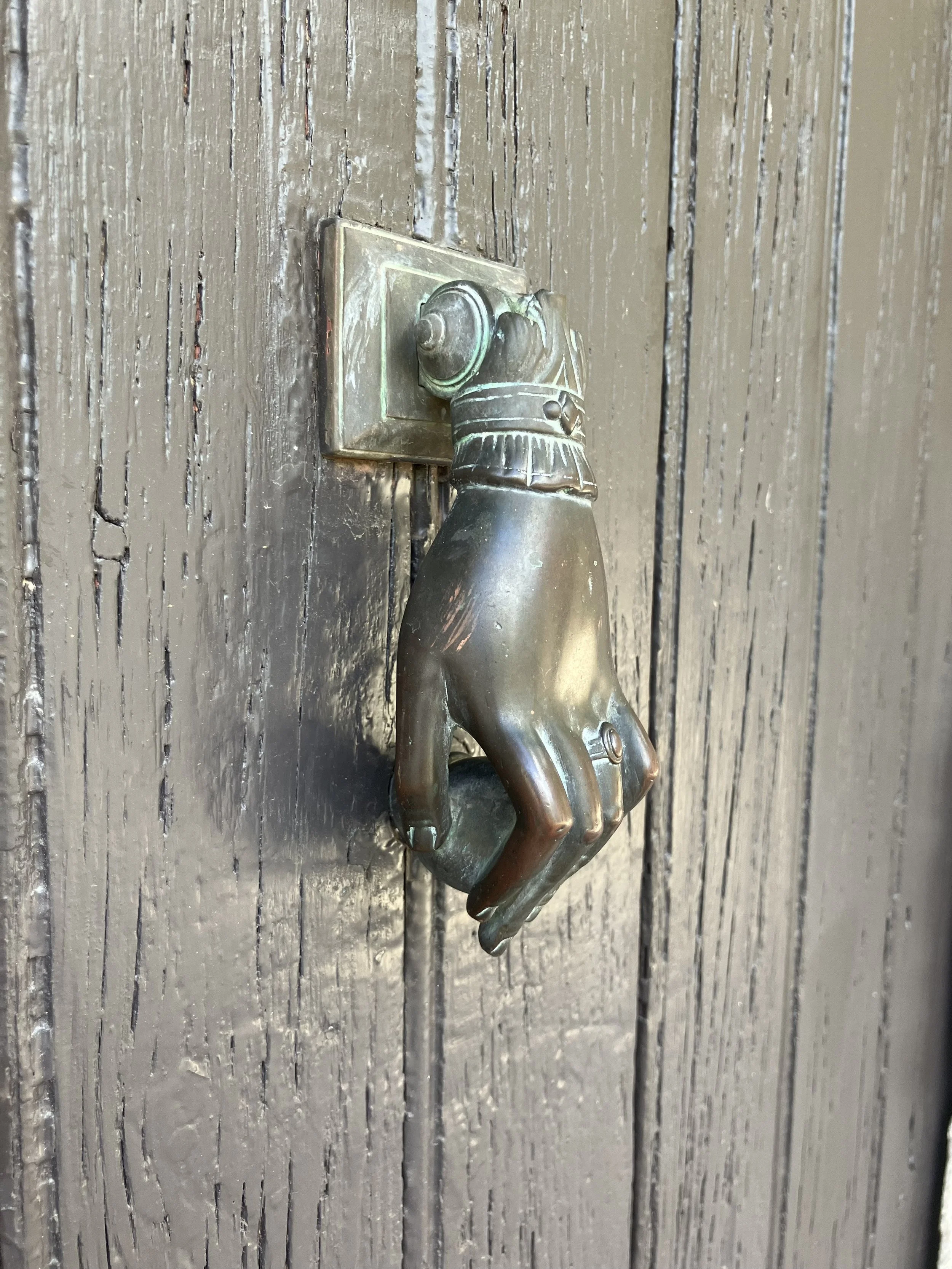 A door handle shaped like a hand, attached to a wooden door with vertical planks.