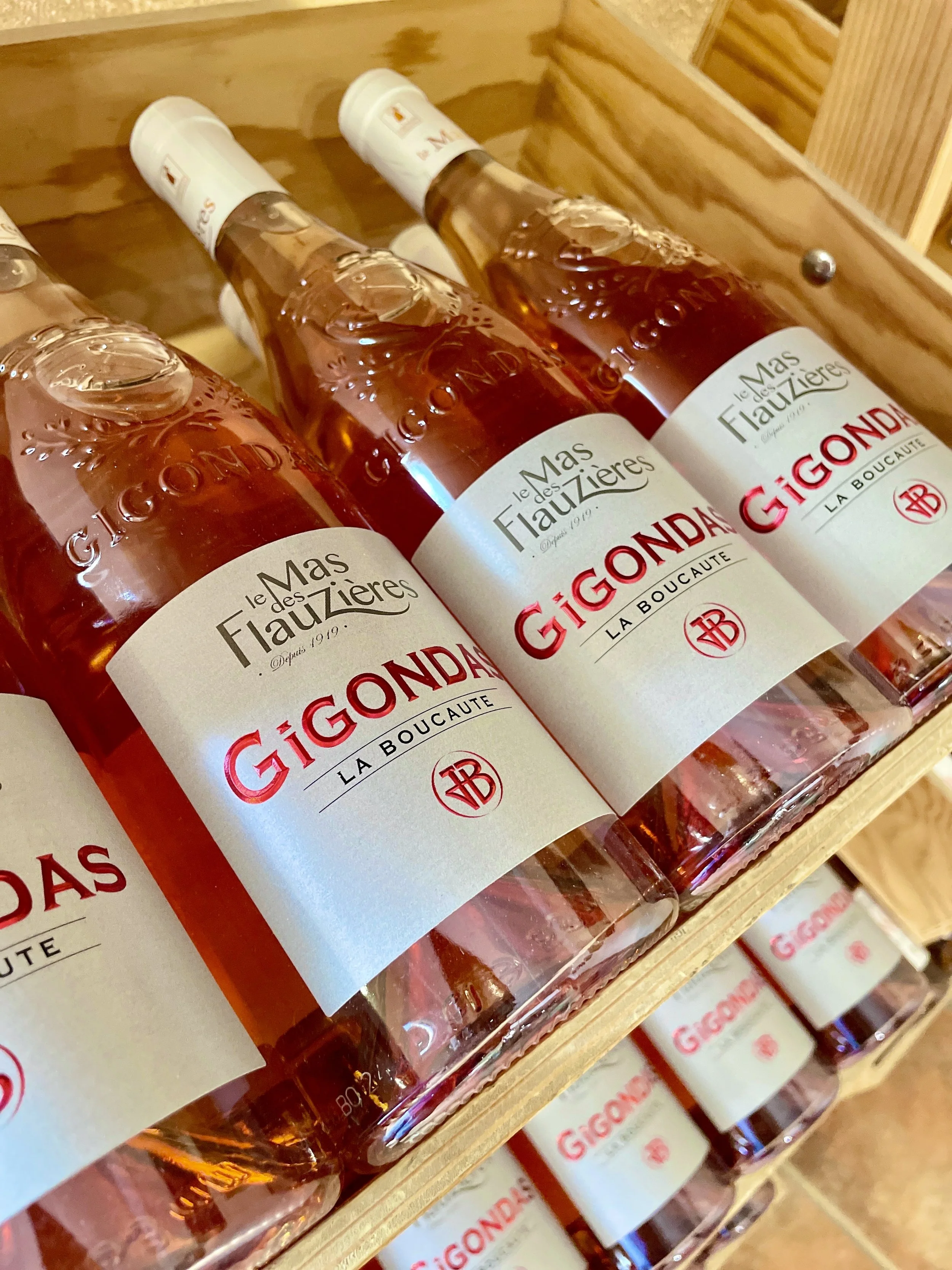 Multiple bottles of Gignons rosé wine on a wooden shelf.