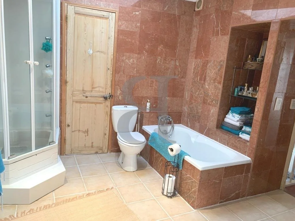 Bathroom with a corner shower stall, toilet, and bathtub with blue towels and toiletries on shelves