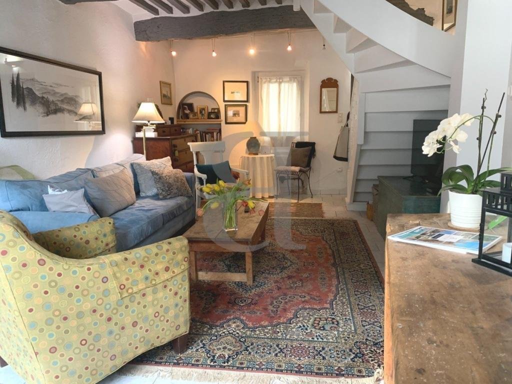 Cozy living room with a yellow polka dot armchair, a blue sofa, a wooden coffee table with a vase of flowers, an ornate area rug, a framed picture on the wall, a side table with a lamp, and a staircase leading to an upper level.