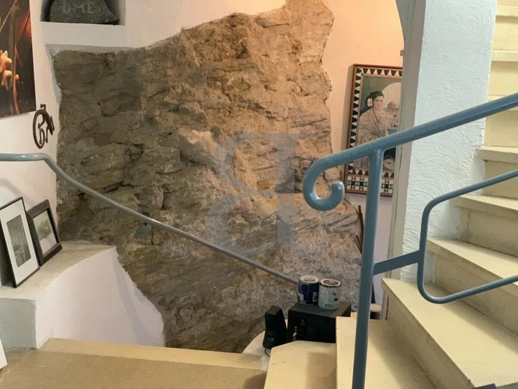 Indoor staircase with a blue handrail leading to a southwestern-style interior, featuring a stone wall, framed artwork, and decorative items.