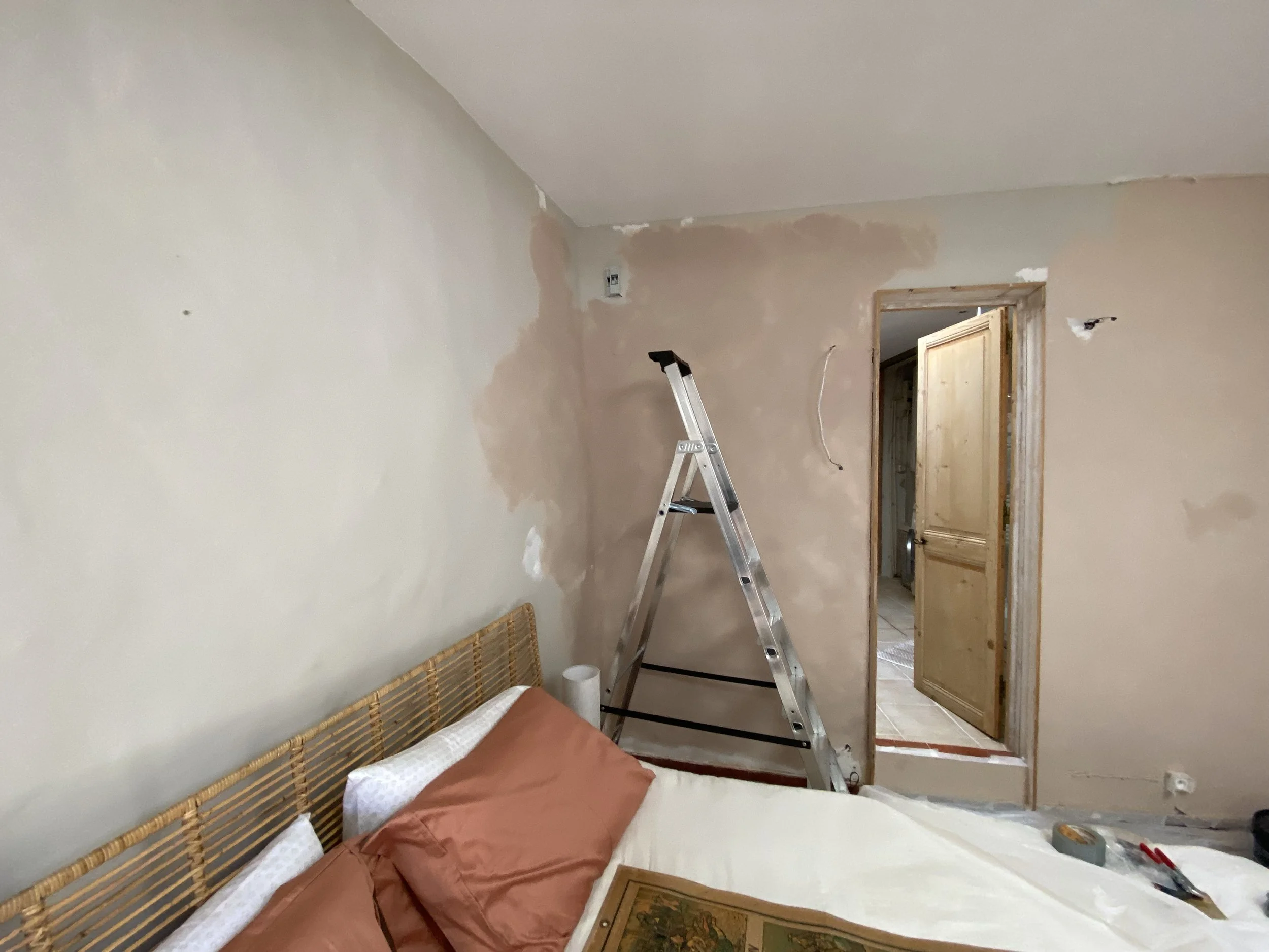 Interior of a room under renovation with unfinished drywall, a ladder, and furniture covered with a blanket.