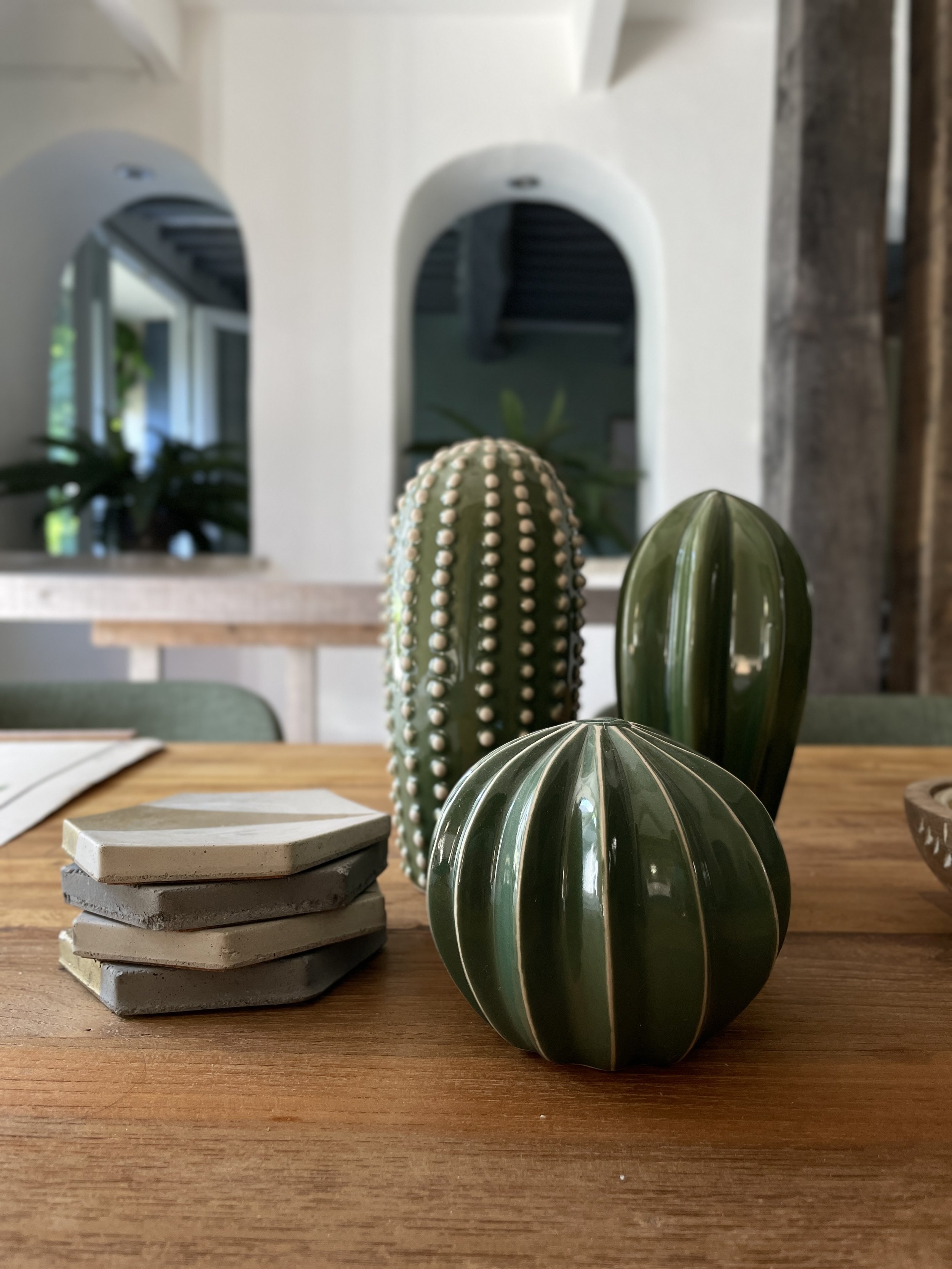 Stacked concrete tiles, artificial cactus plants, and a wooden table in a room with mirrored wall and plants.