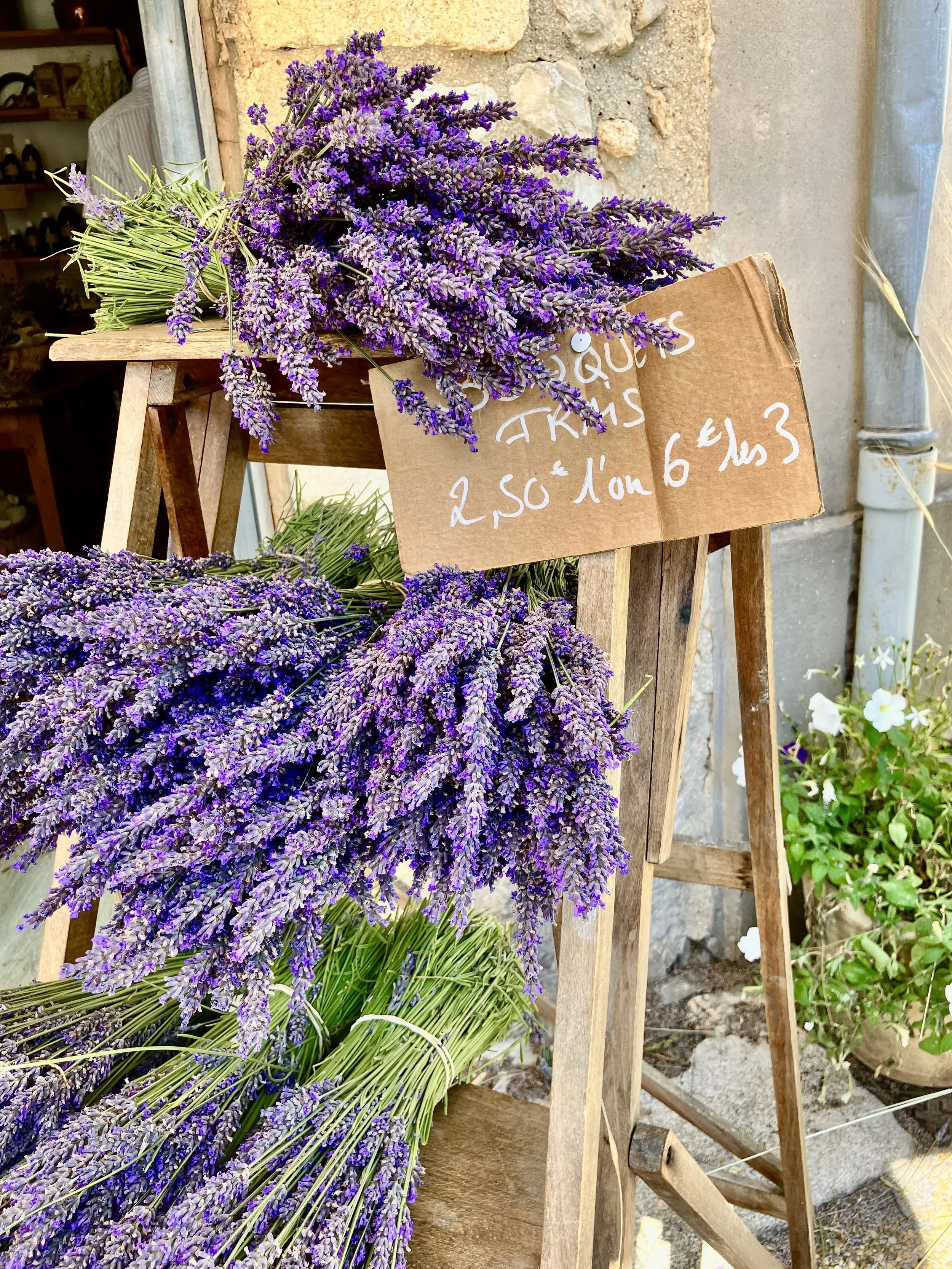 Bundles of fresh lavender flowers with a handwritten price sign in front of a rustic outdoor shop display.