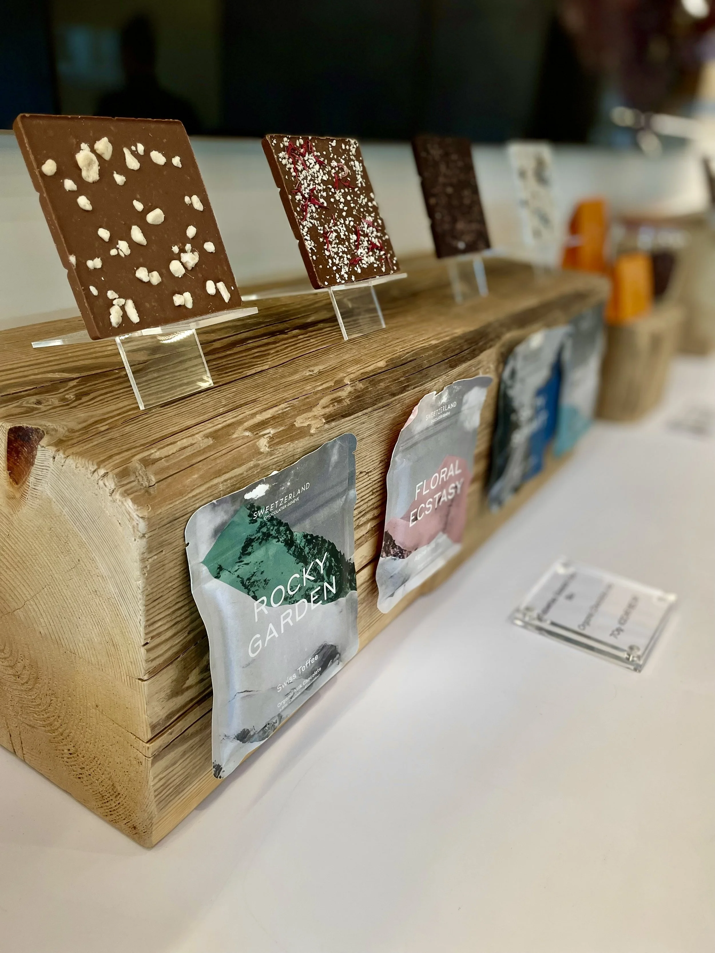 A row of chocolate bars on display, each decorated differently, placed on a wooden stand.