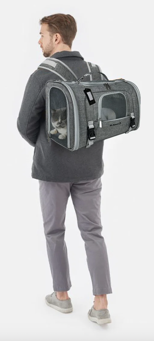 A man carrying a pet carrier backpack with a black and white cat inside, standing against a plain white background.