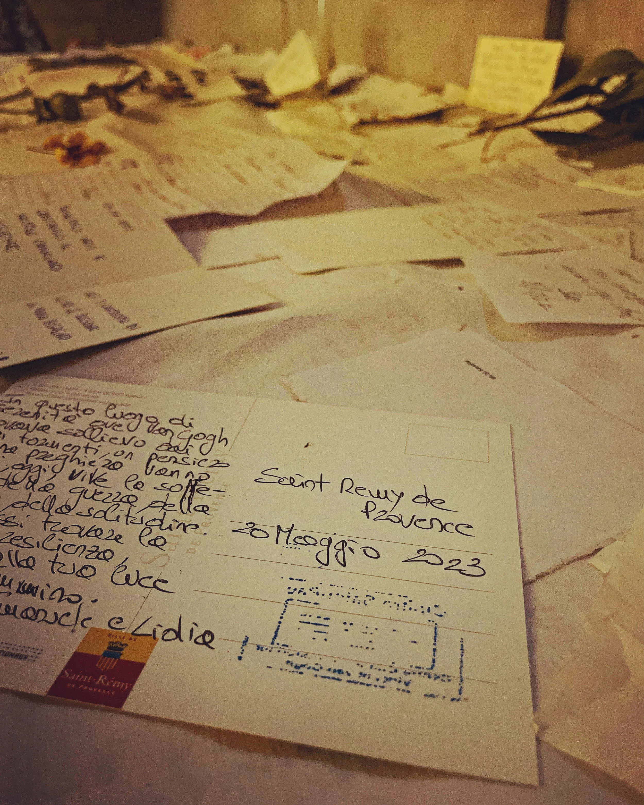 Piles of handwritten notes and papers on a table with a business card and a paper with the title 'Sent Rémy de Provence'.