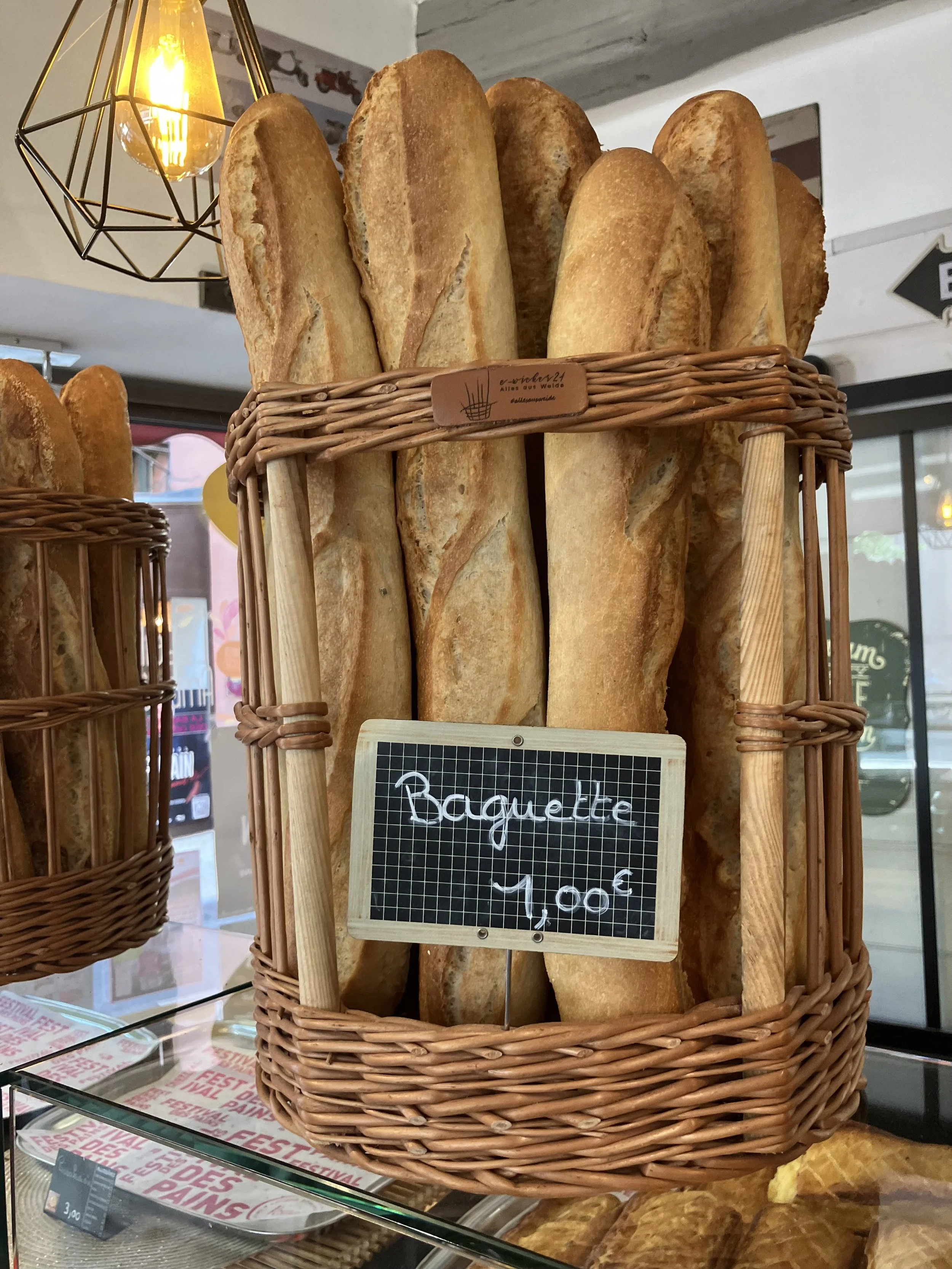 A basket of baguettes on display in a bakery, with a handwritten sign indicating the price of 1.00 euro.