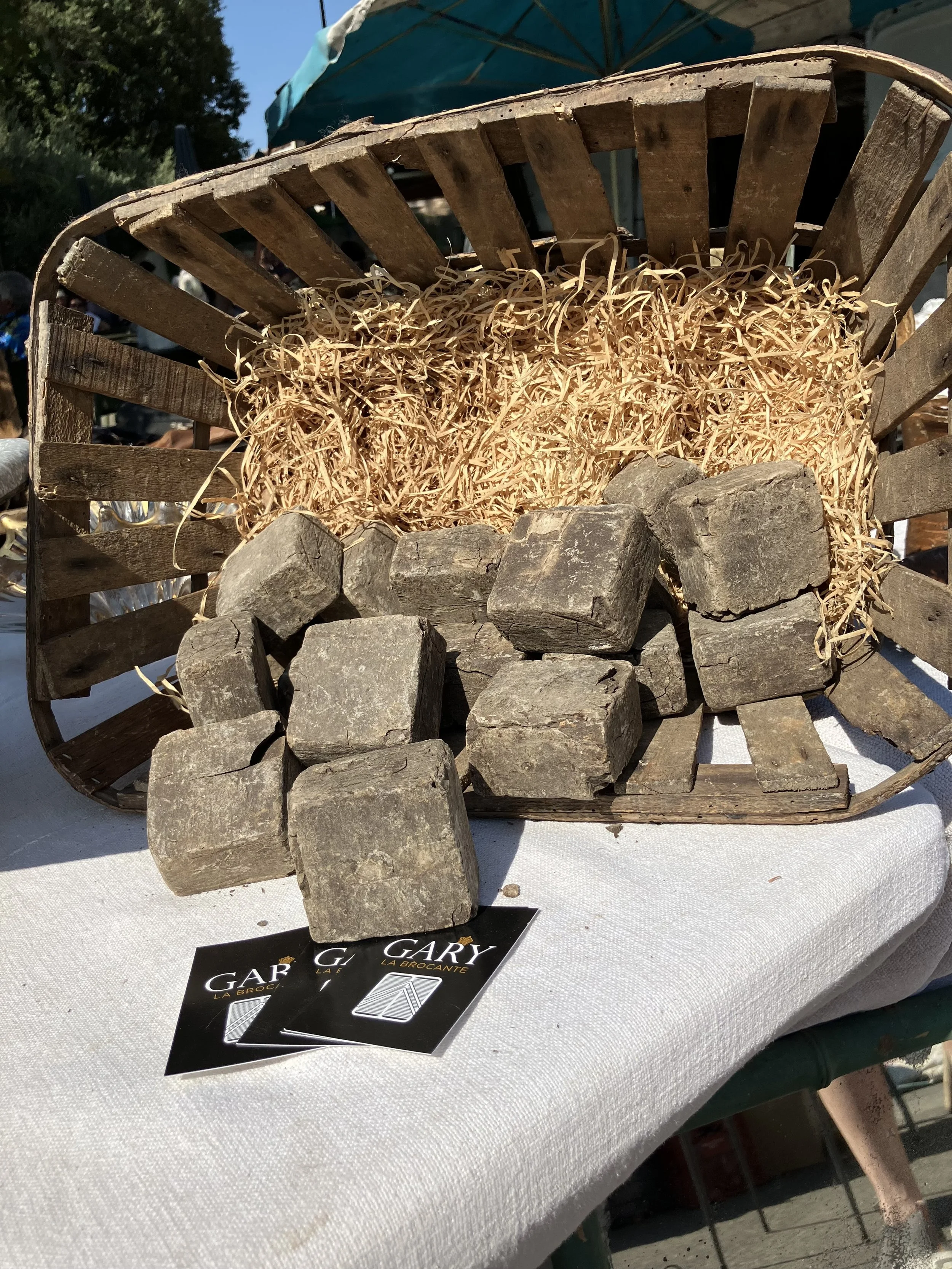 A wooden cart filled with straw and gray stones, placed on a white cloth table at an outdoor market.