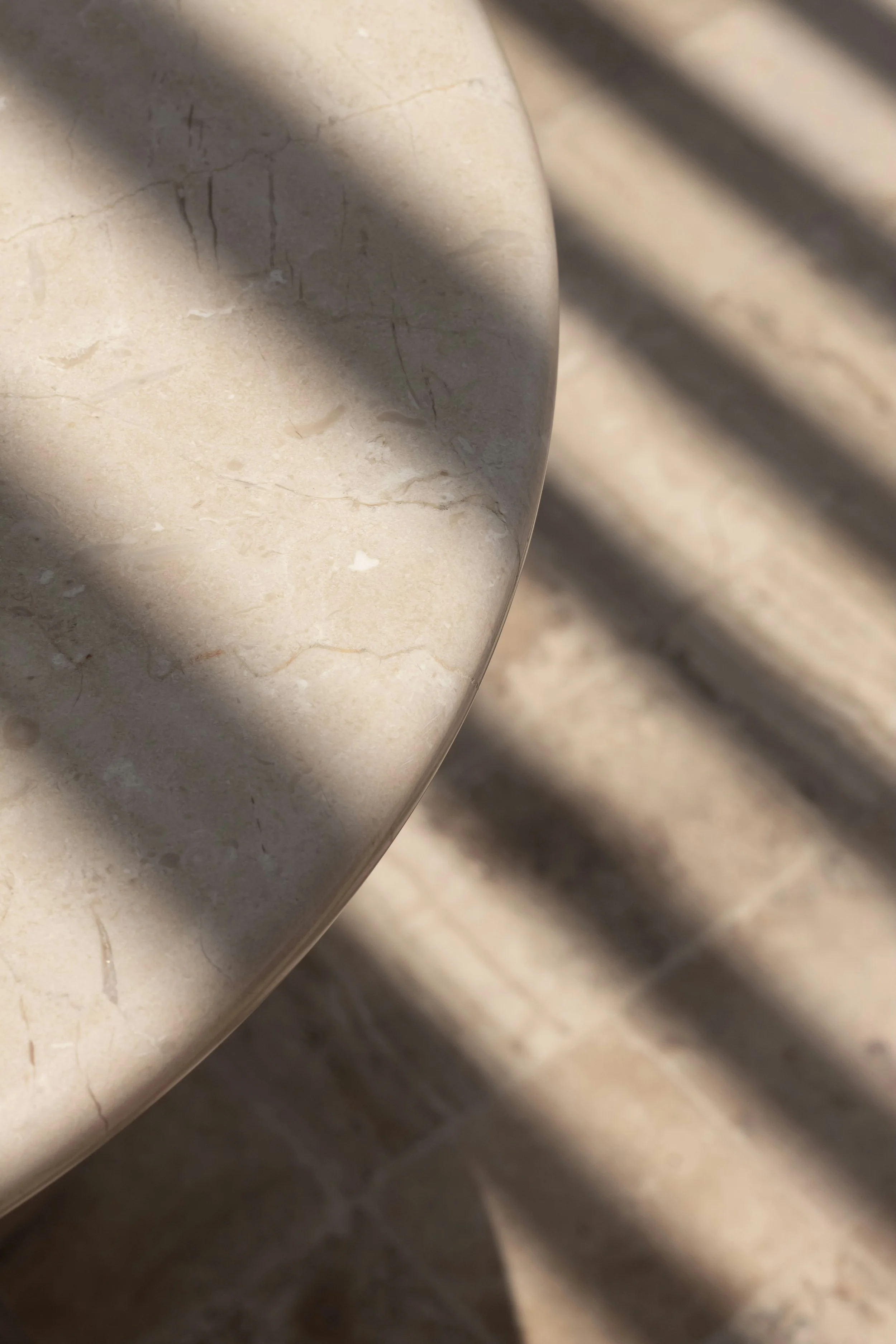 Close-up of a beige marble surface with visible veins and cracks, and shadows cast across it.