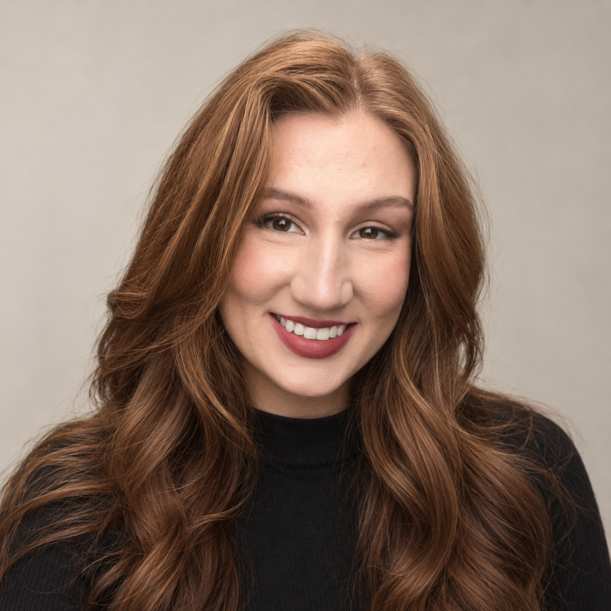 Portrait of a red-haired woman smiling, wearing a black top, against a light grey background.