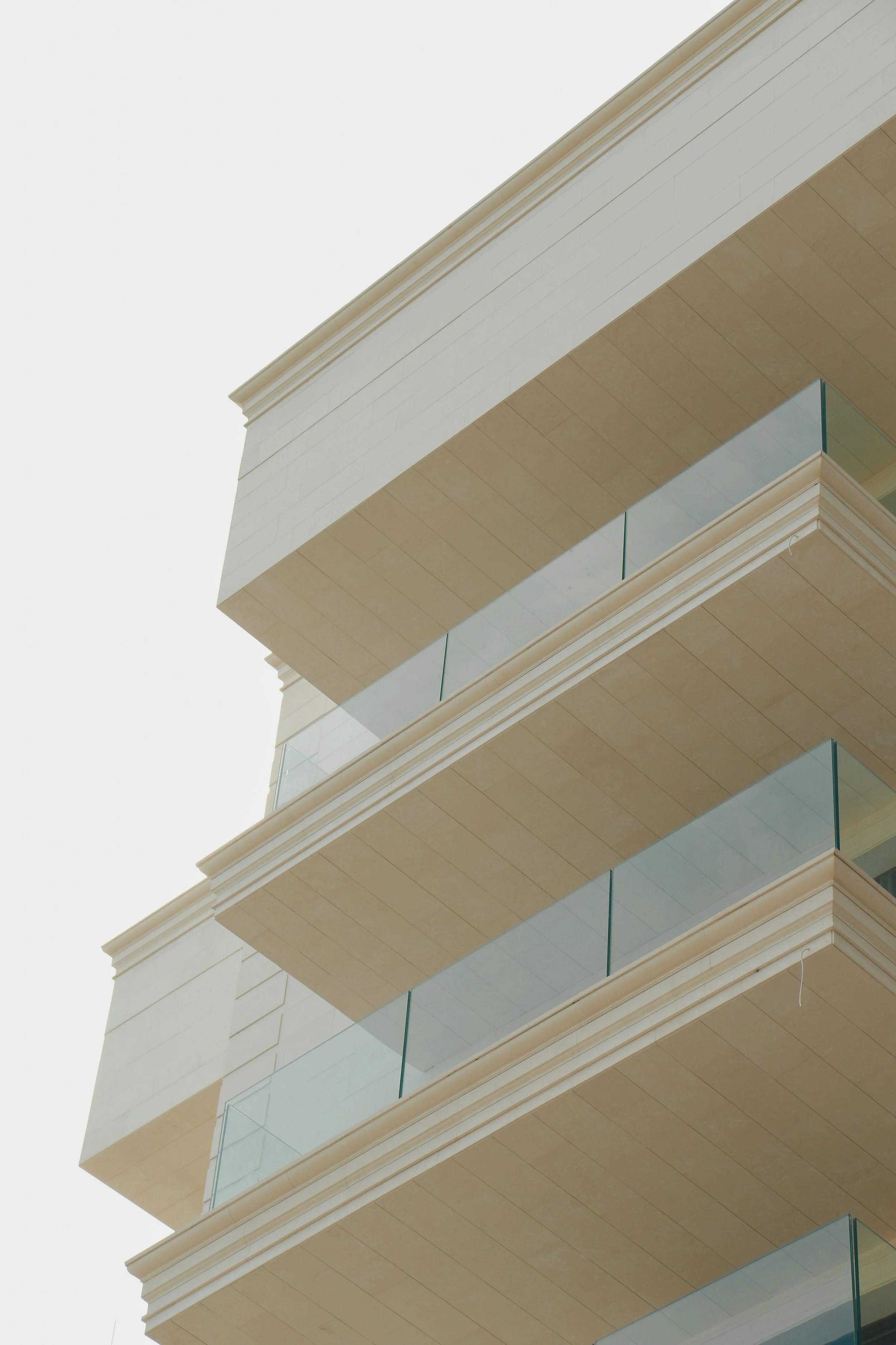 A multi-story modern apartment building with glass balcony railings, beige walls, and detailed molding at the corners.