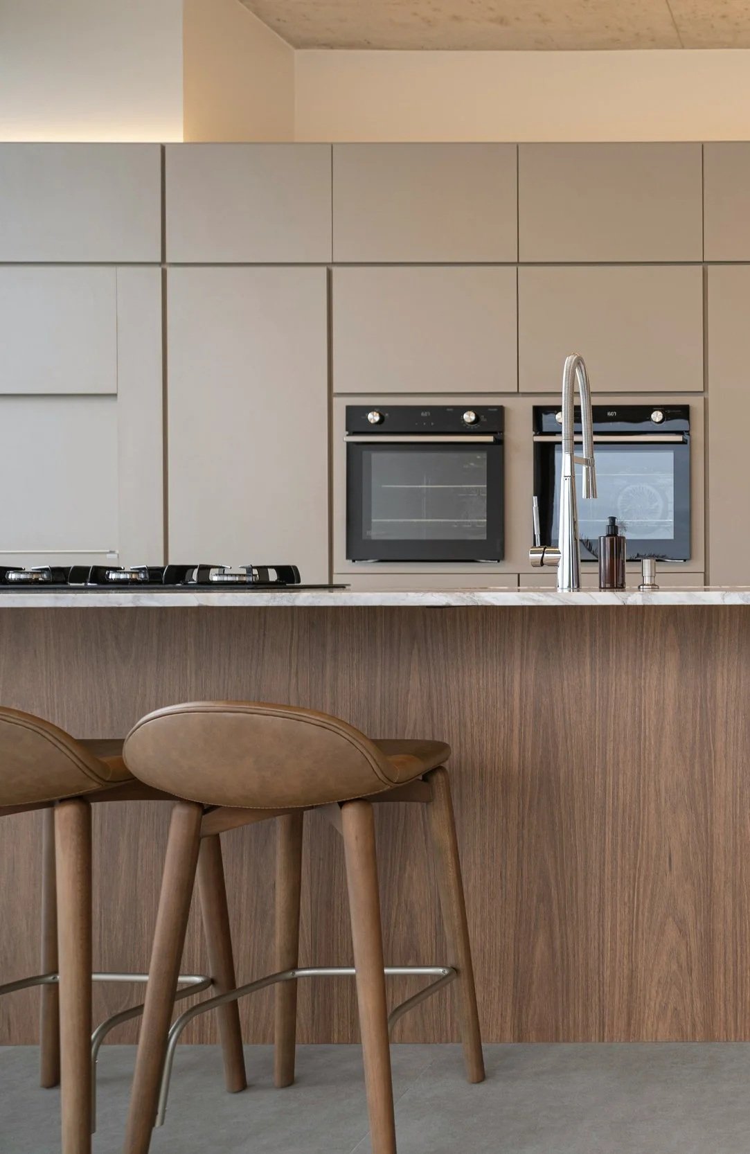 Modern kitchen with built-in ovens, a marble countertop, a wooden kitchen island, and beige cabinetry.