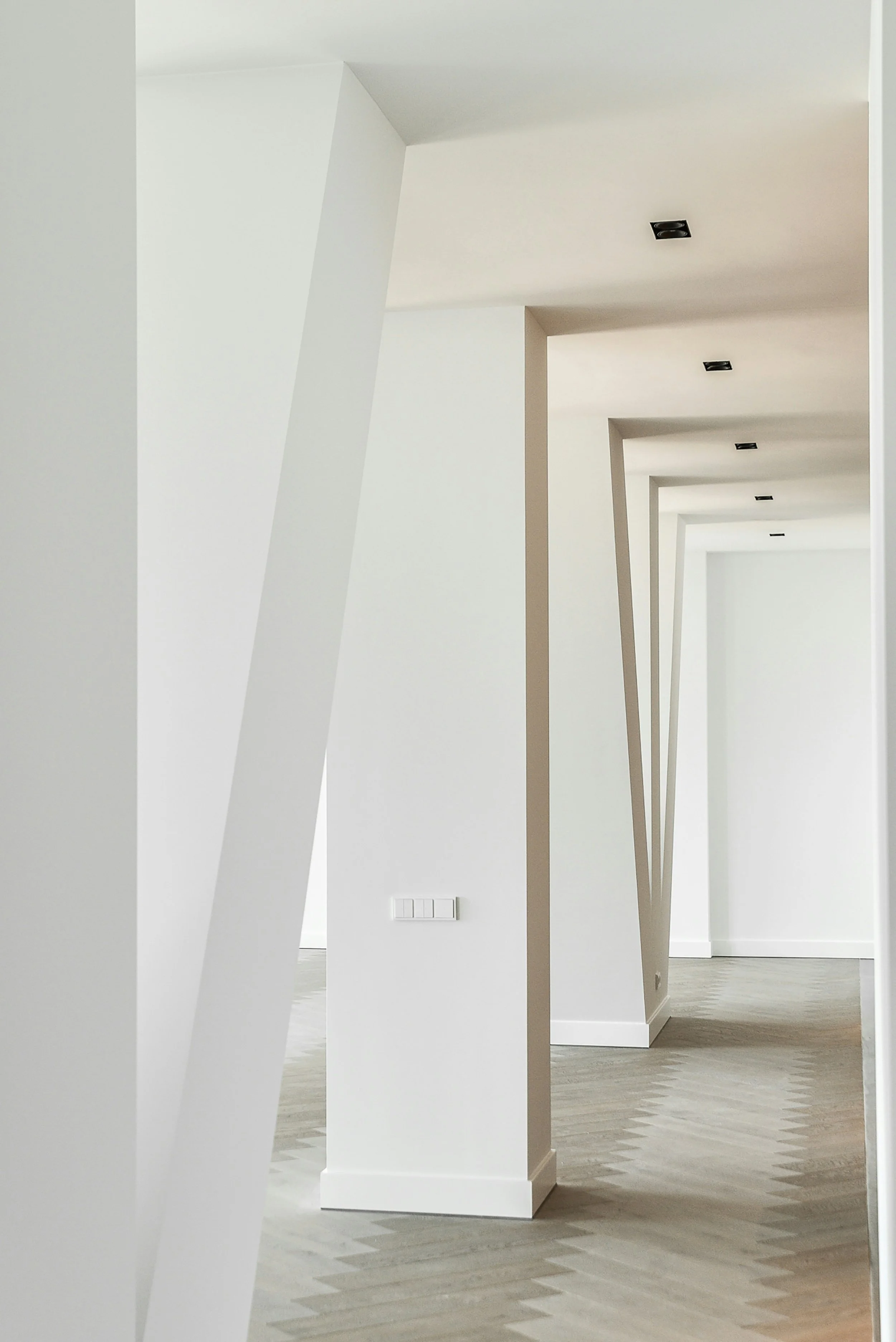 Minimalist interior with white walls, geometric wall designs, light wood flooring, and black ceiling spotlights.
