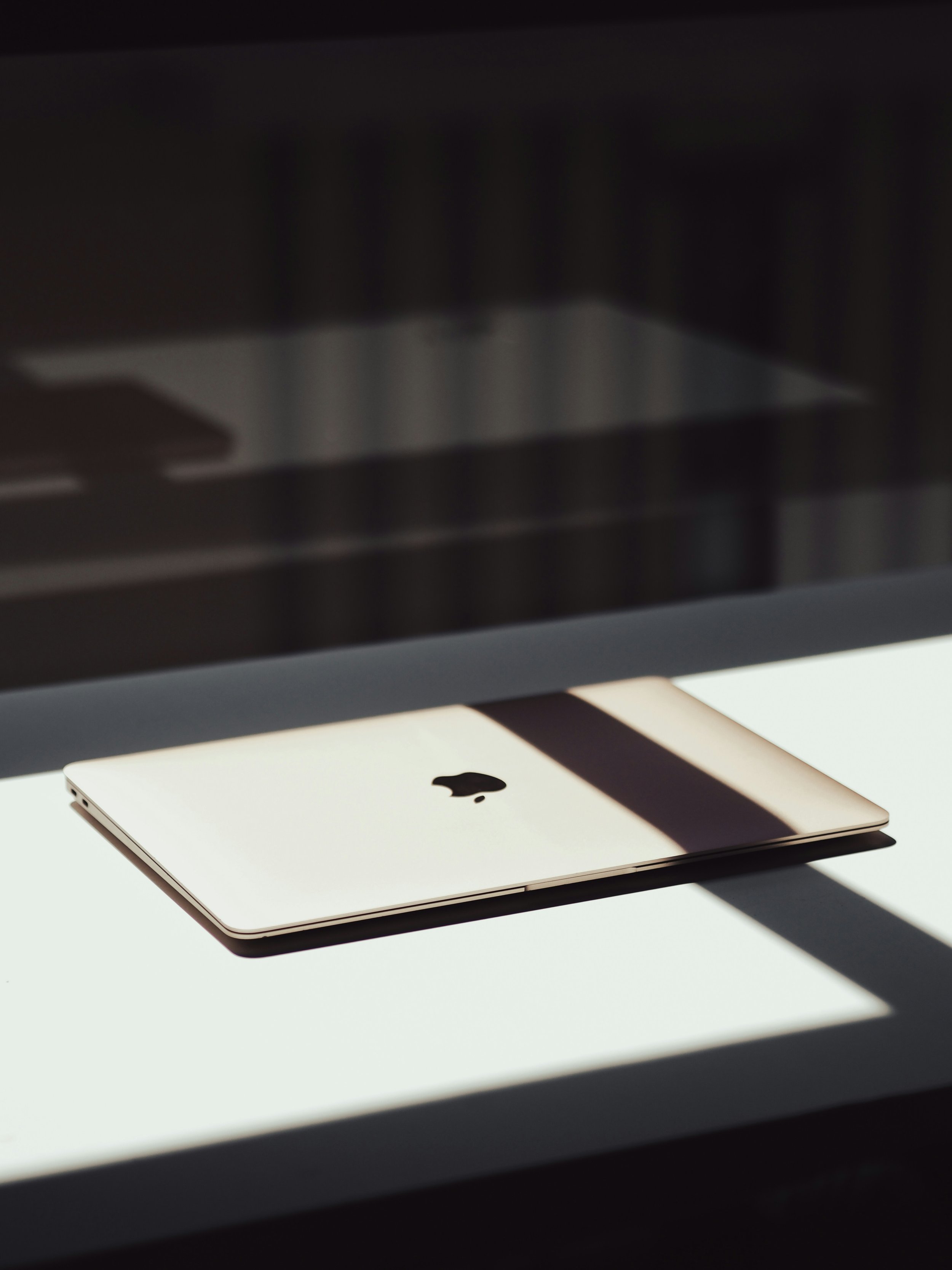 A closed silver MacBook laptop on a white surface with sunlight casting shadows.