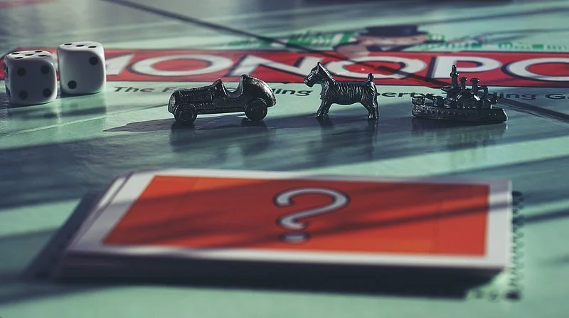 Monopoly game with dice, miniature cars, horse, boat, and a question card on the board.