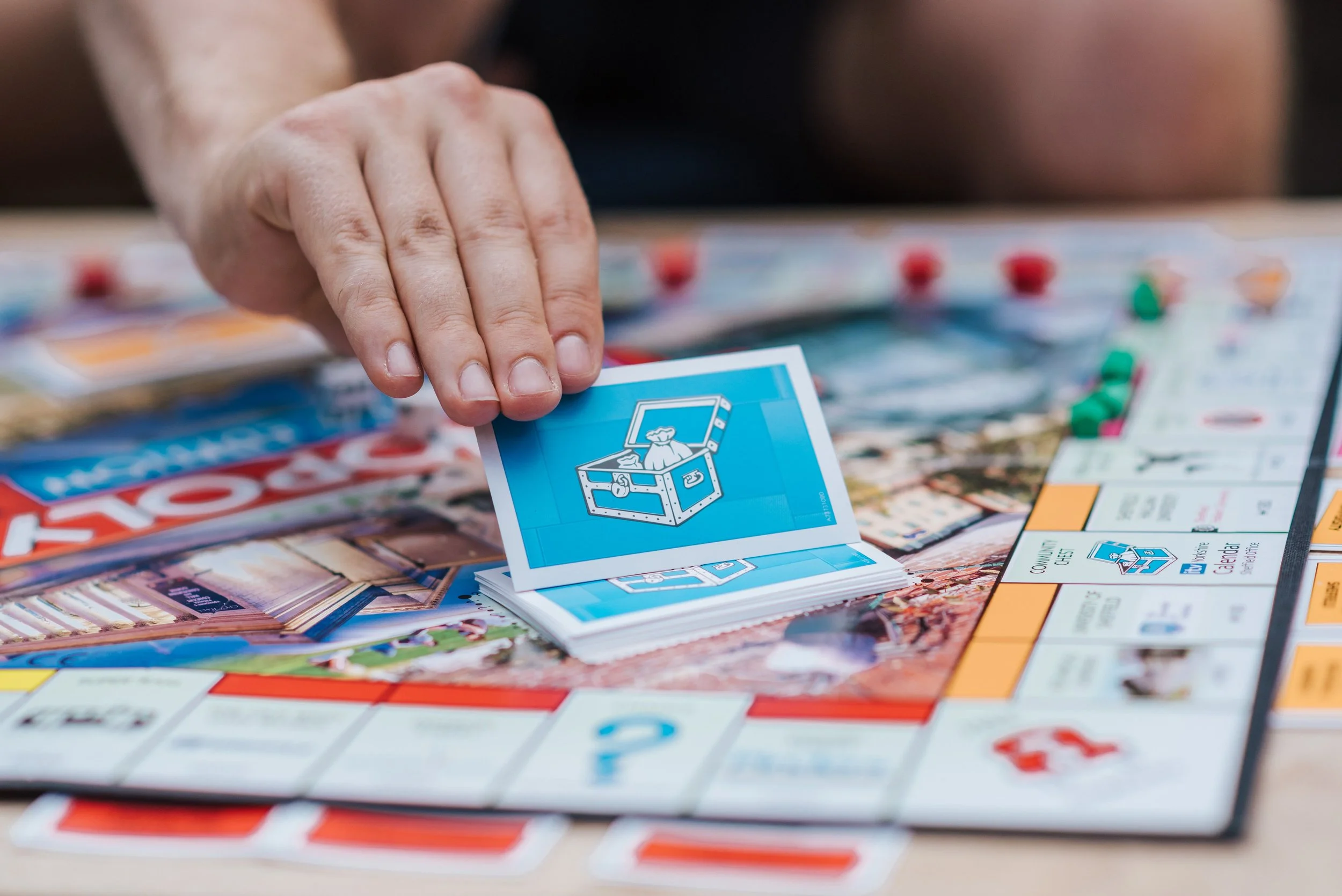 Close-up of a person's hand dropping a blue 'Community Chest' card onto a Monopoly game board.