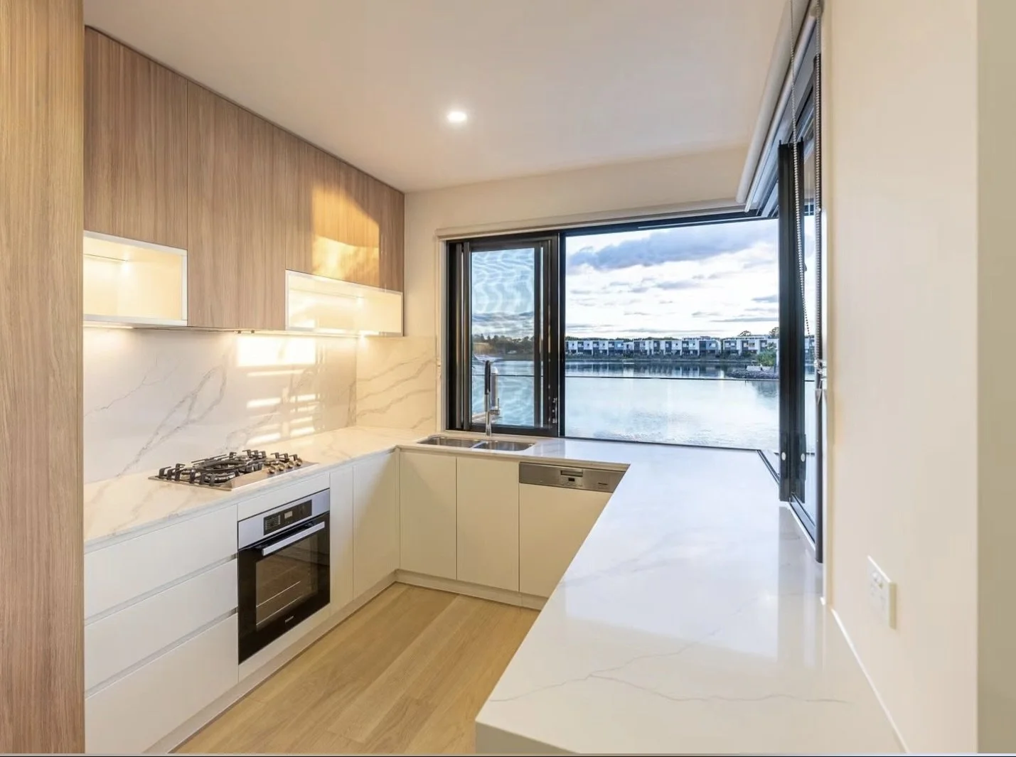 Modern kitchen with white marble countertops, a built-in oven, gas stove, and a large window with a view of a river and buildings outside.