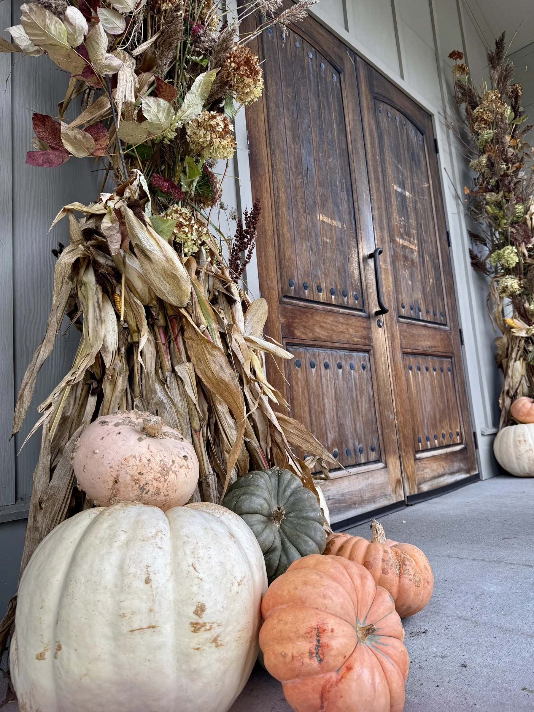 Custom fall porch by Home & Hydrangea: dried hydrangea and cornstalk arrangements with heirloom pumpkins beside wooden double doors