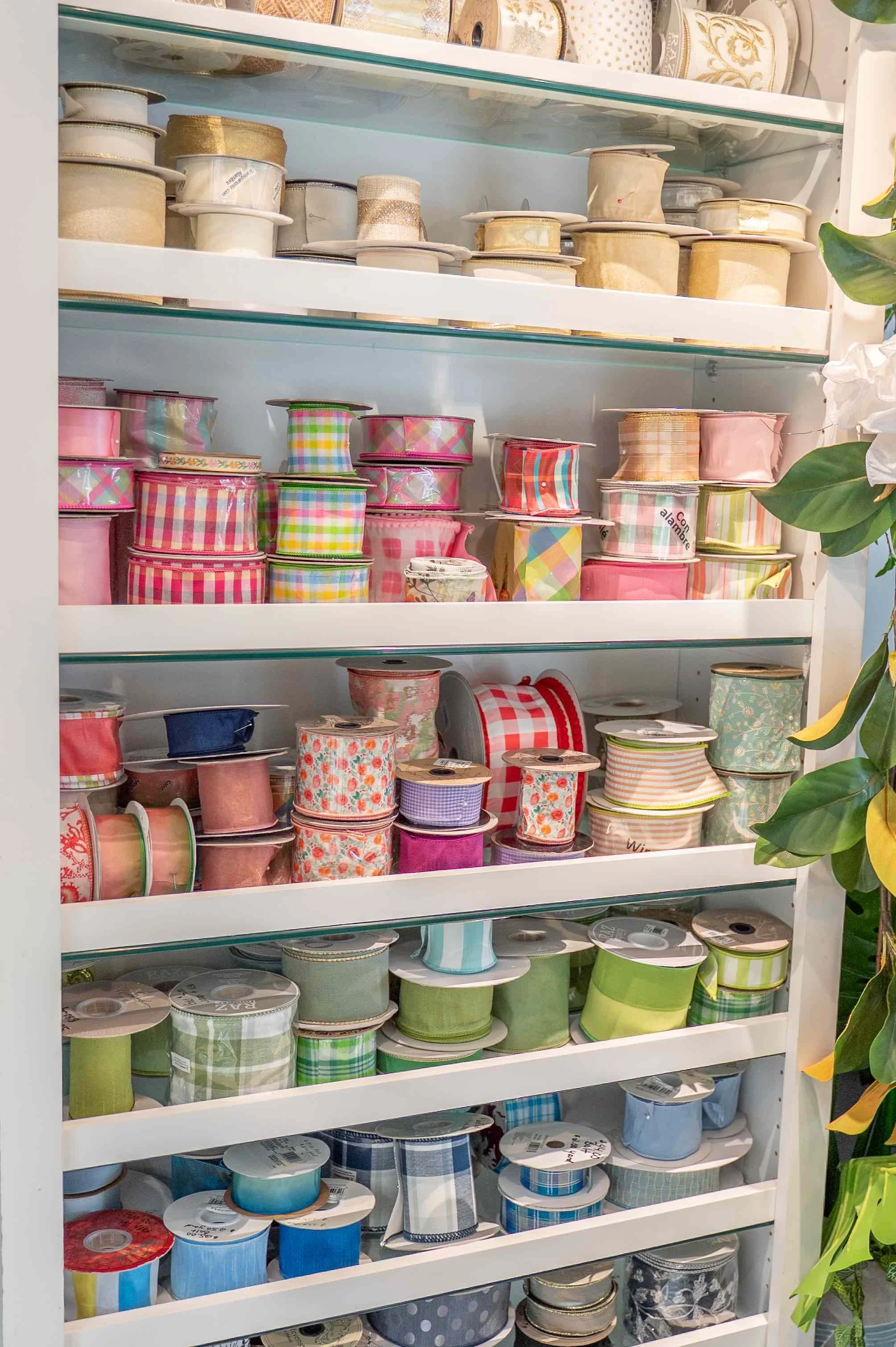 A display shelf filled with colorful spools of ribbon arranged by color, including gold, pink, red, green, blue, and black.