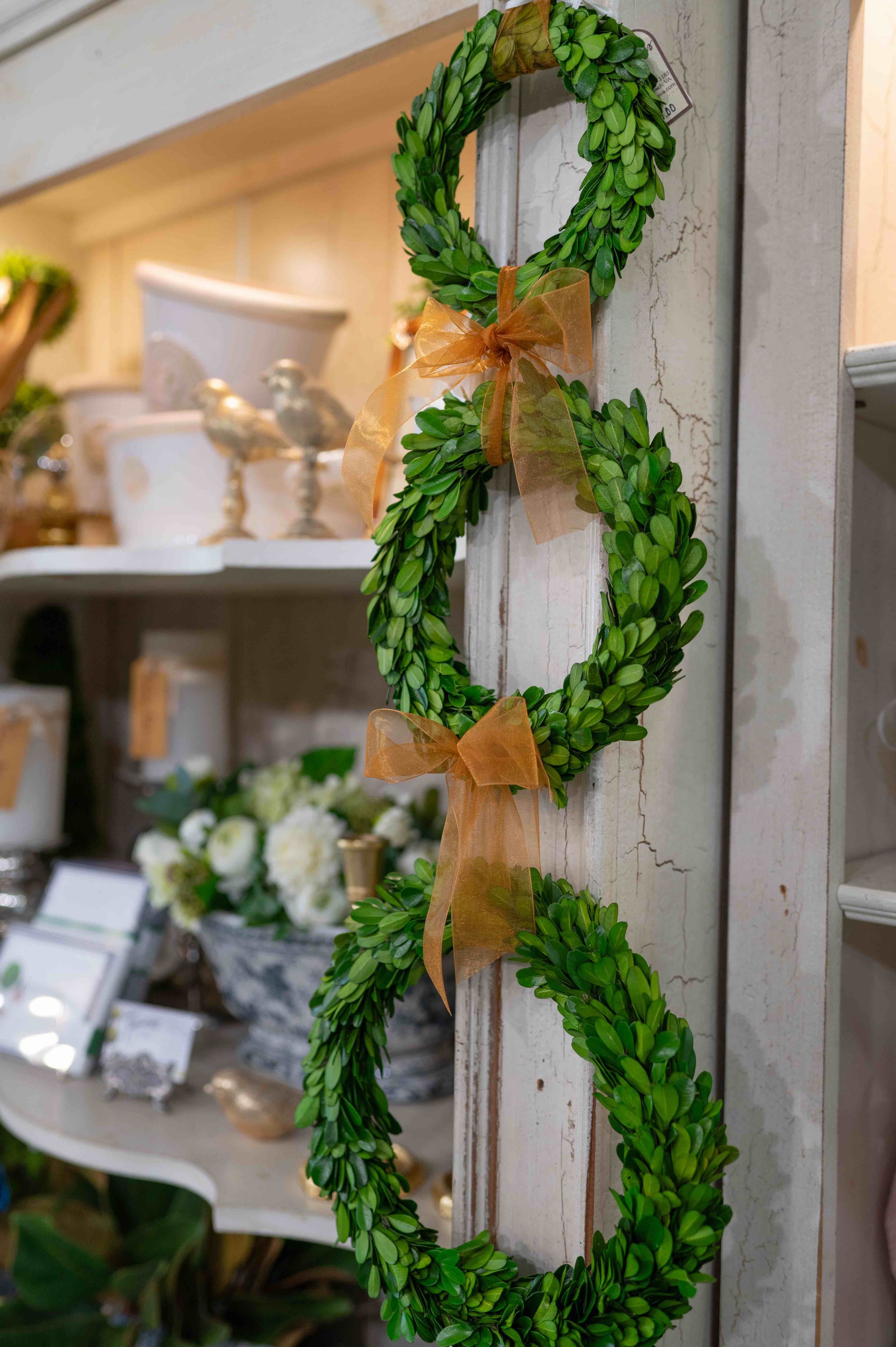 A decorative green wreath with brown ribbons hanging on a rustic wall.