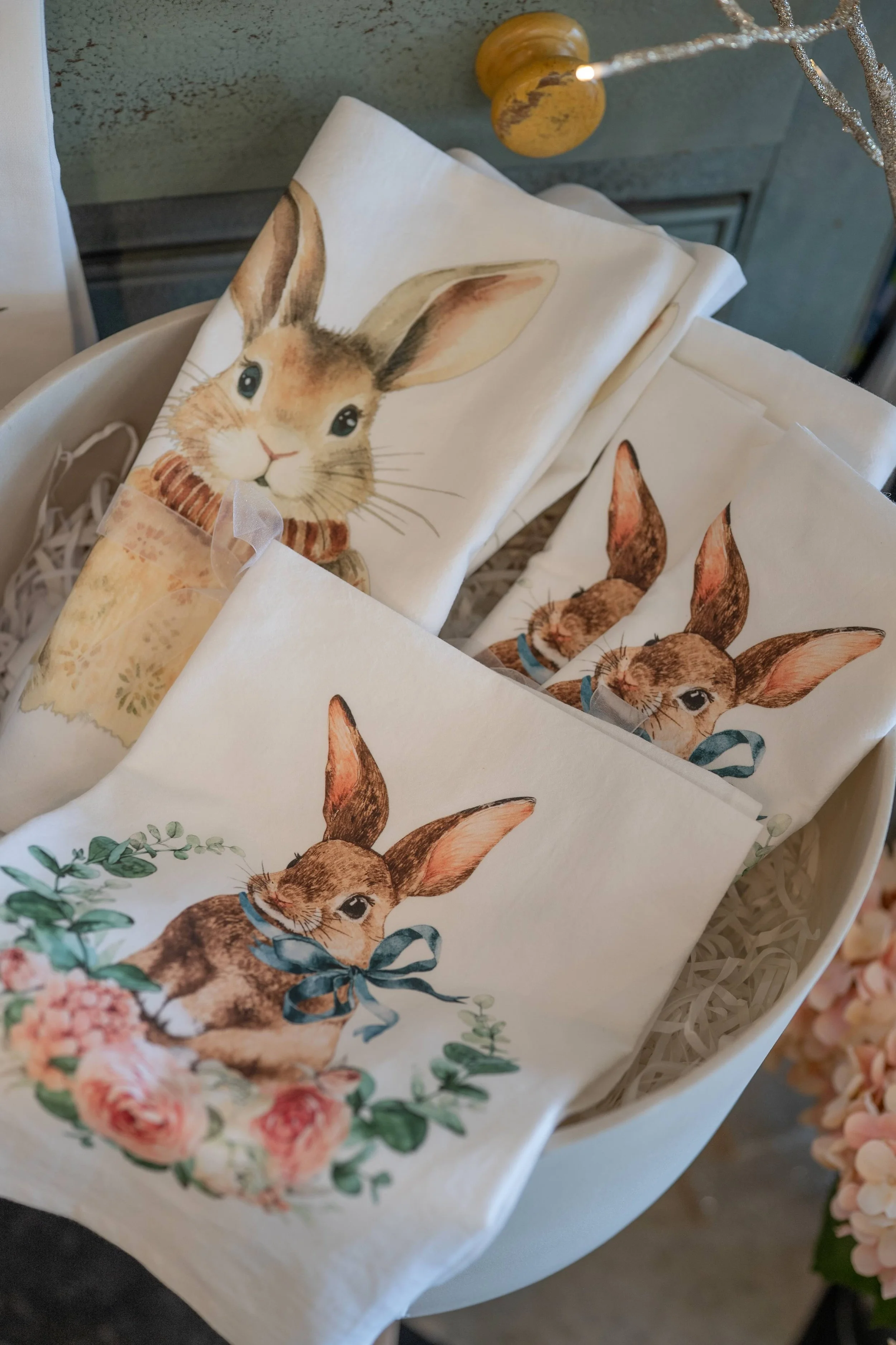 Decorative napkins with watercolor illustrations of rabbits, one with a light brown bunny with big ears and another with a darker bunny wearing a ribbon, arranged in a basket.