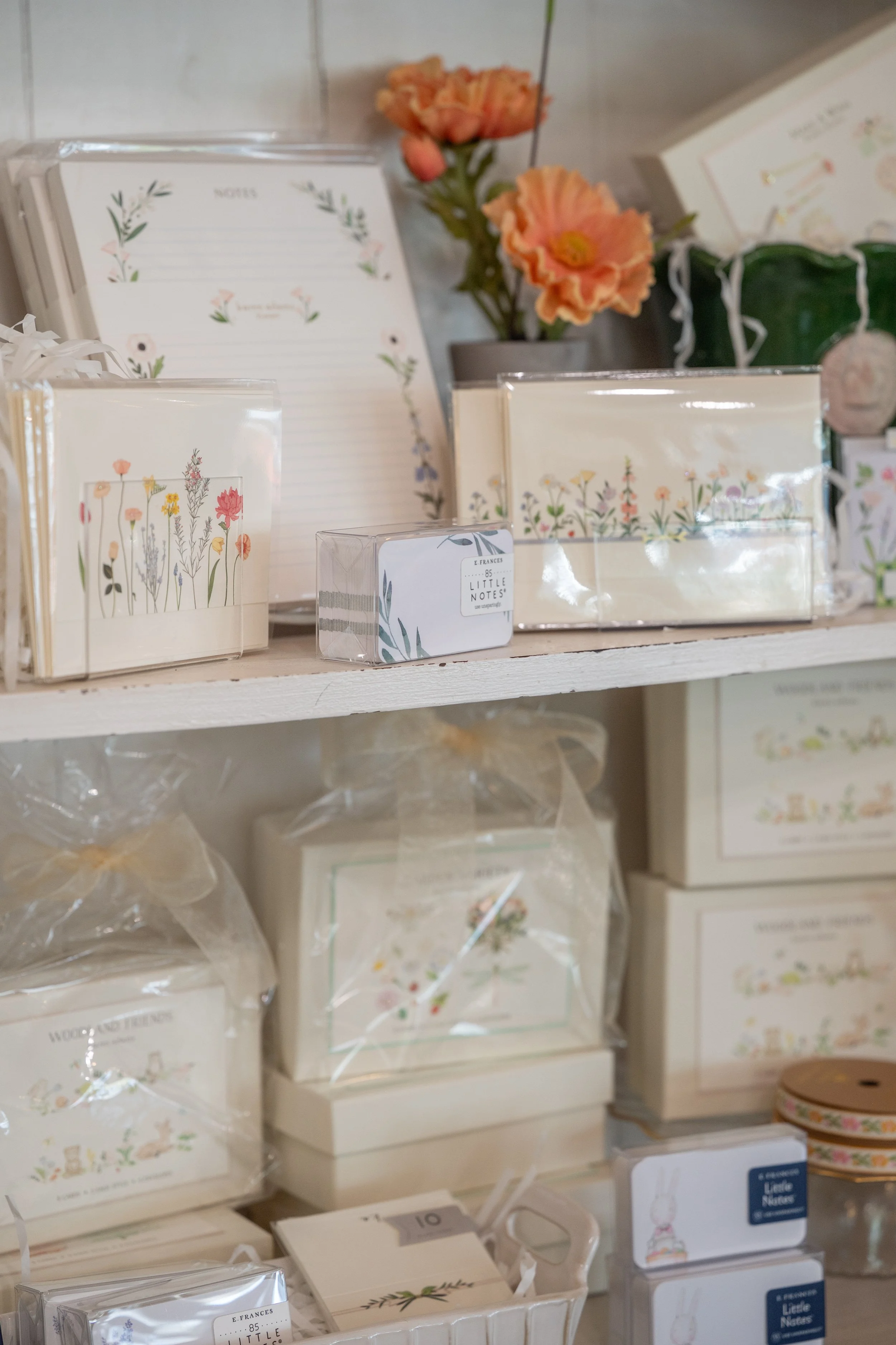 Display of floral-themed stationery, boxes, and notebooks with pastel colors and botanical designs, arranged on a shelf.