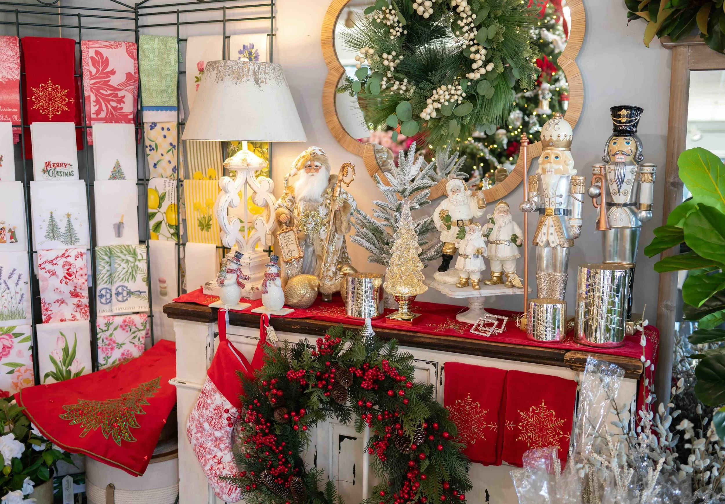 A retail display of Christmas holiday decorations including figurines of Santa Claus and nutcrackers, a small frosted Christmas tree, various ornaments, and holiday-themed textiles in the background.