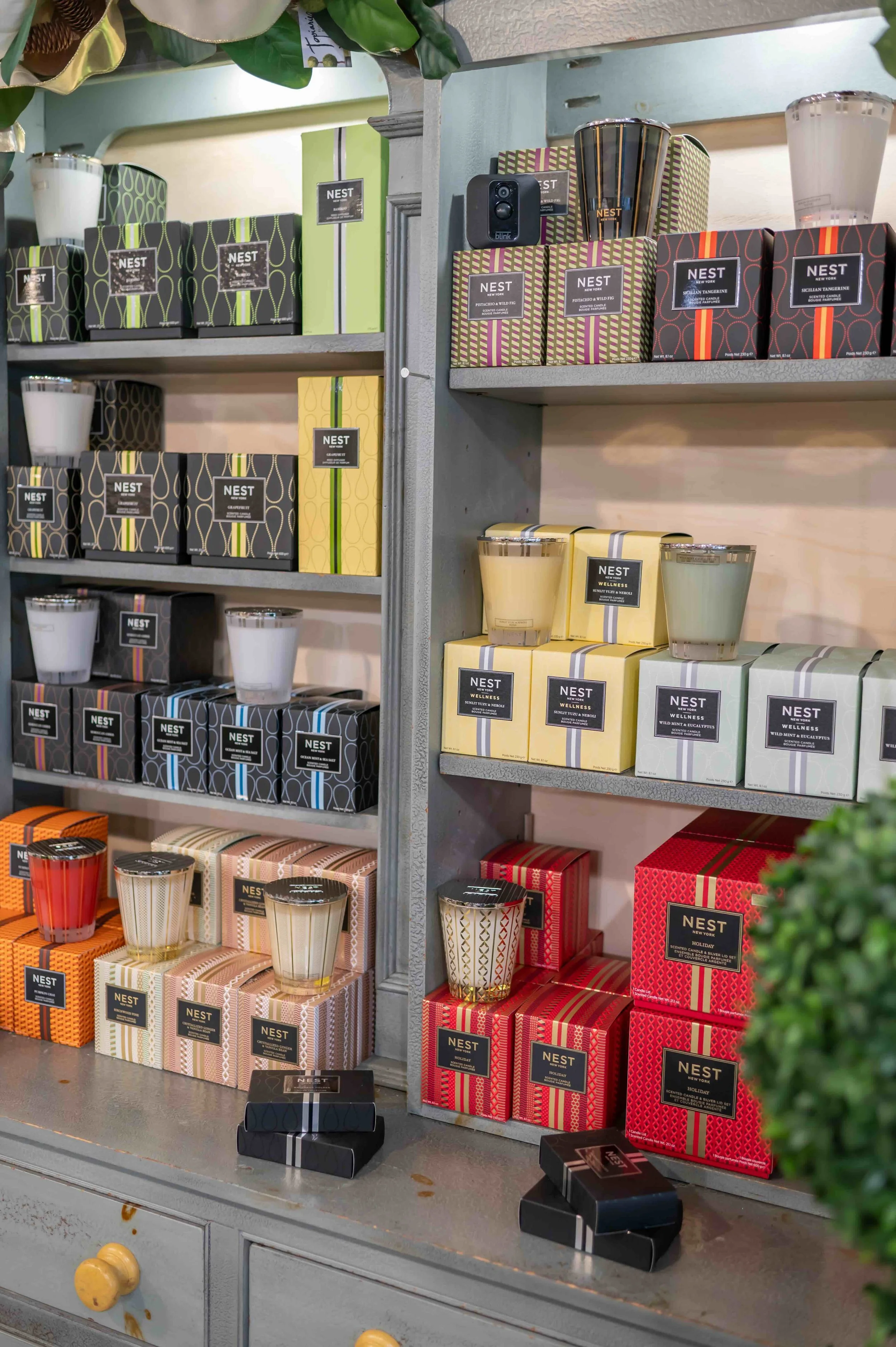 Shelf display of various scented candles in colorful, patterned boxes, with some candles outside their packaging in front, in a retail setting.