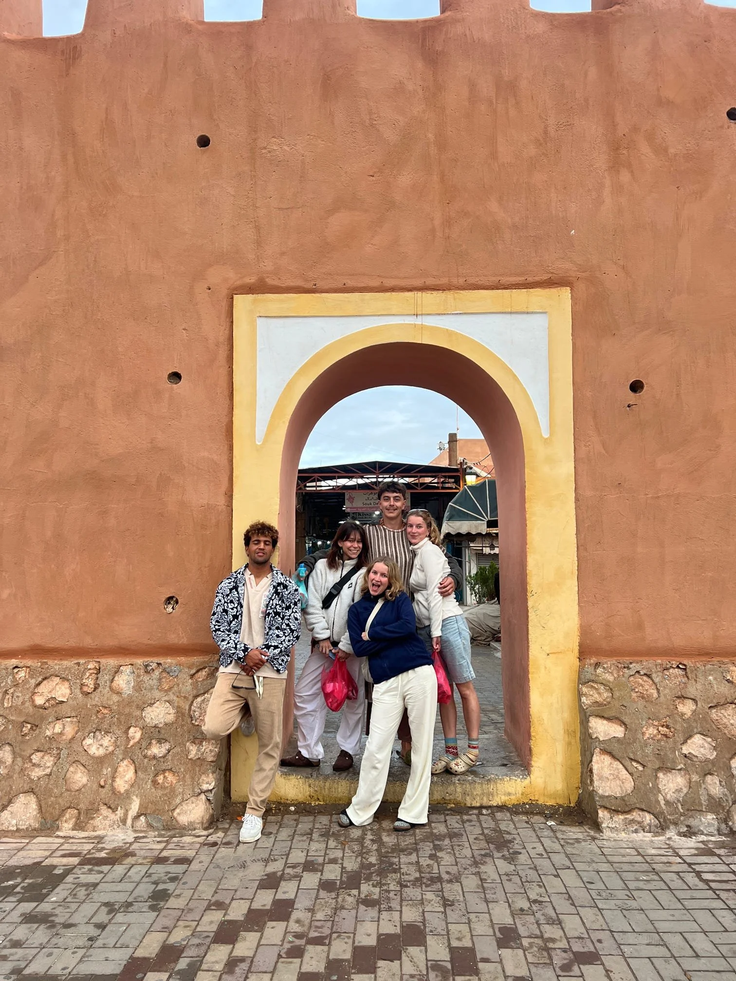A group young adults posing together at an old city archway made of adobe with a stone and brick base.